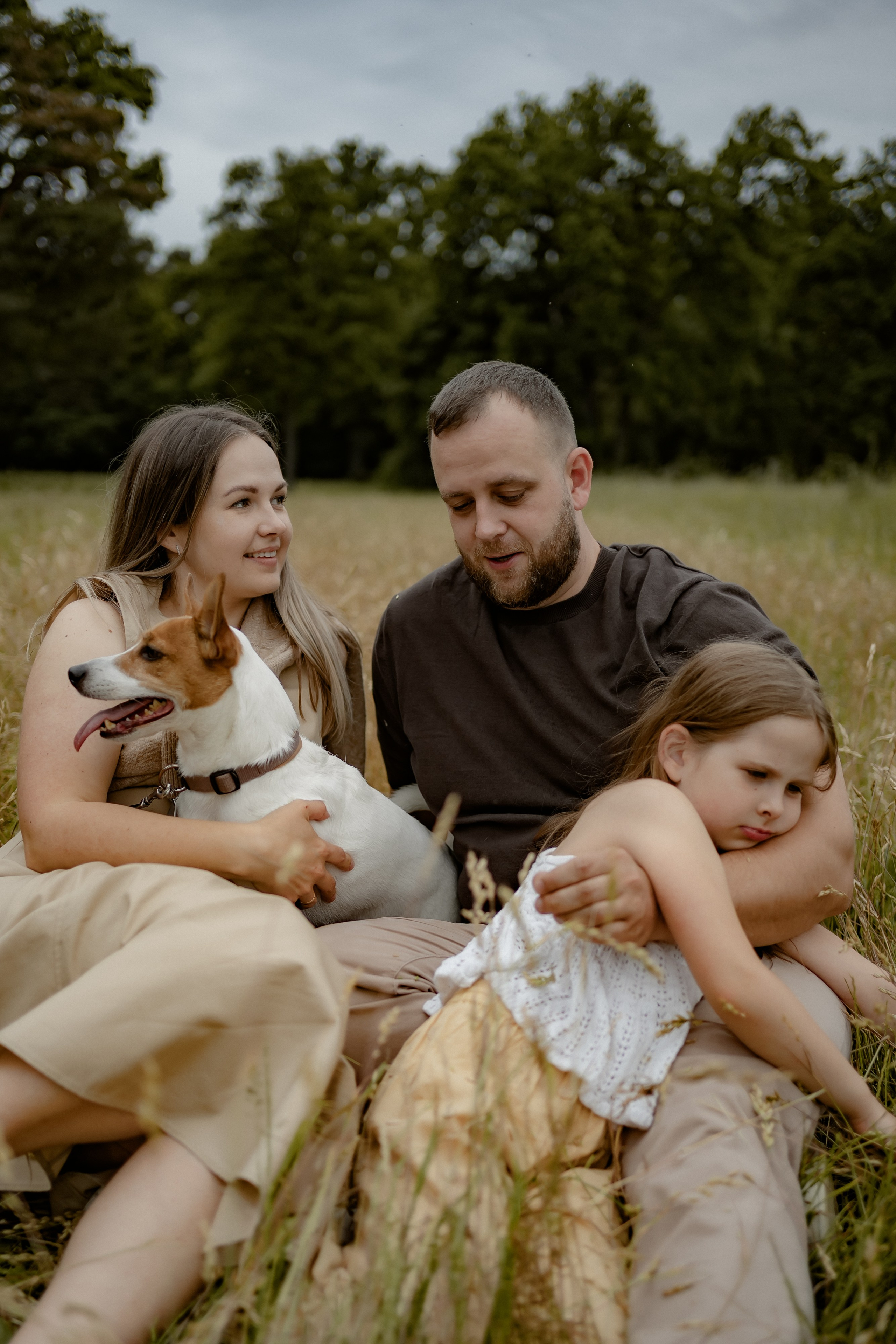 Eltern und Tochter sitzen gemeinsam im hohen Gras und kuscheln bei einem Familienshooting in der Natur.