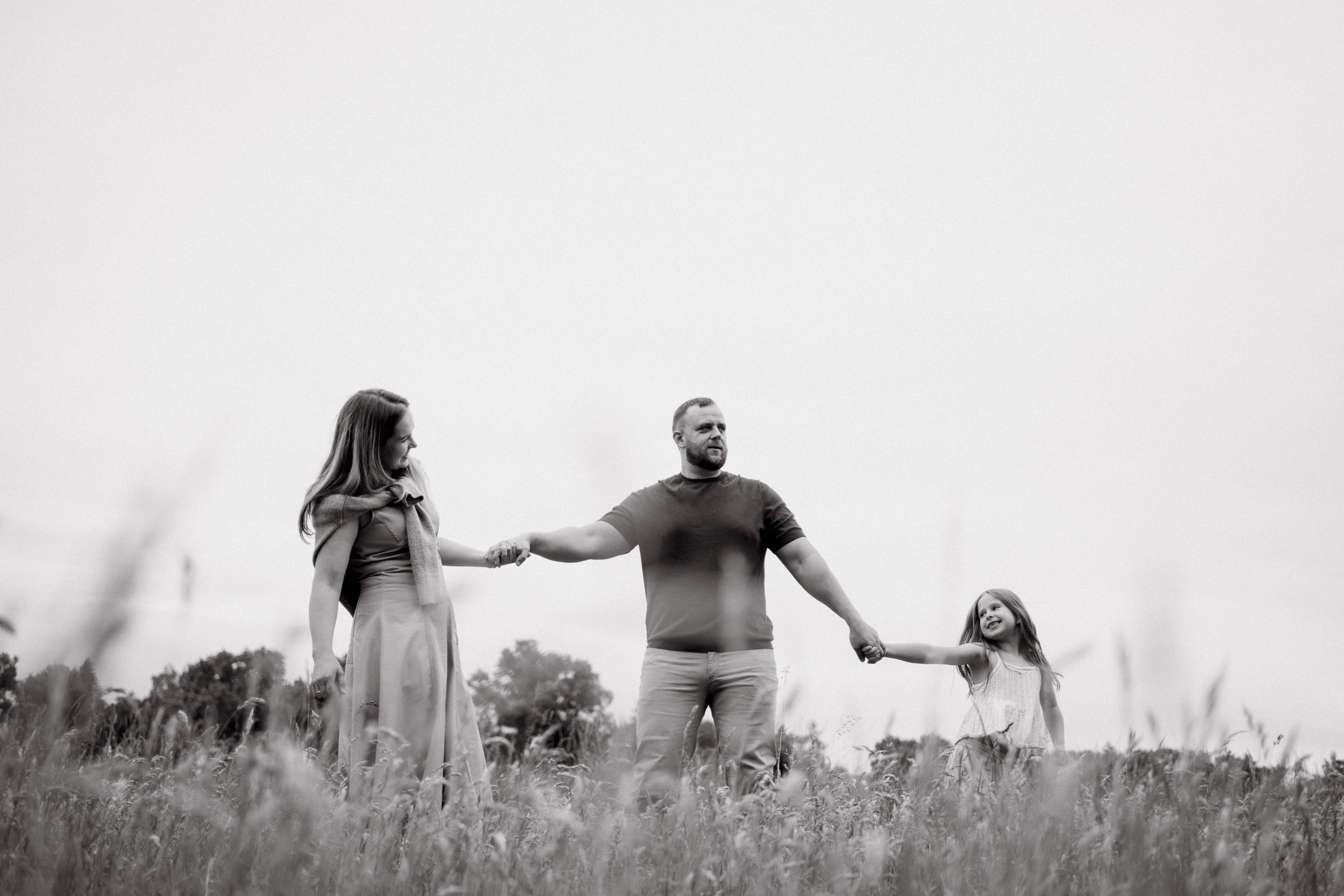 Schwarz-Weiß-Aufnahme einer Familie, die Hand in Hand über eine Wiese läuft.