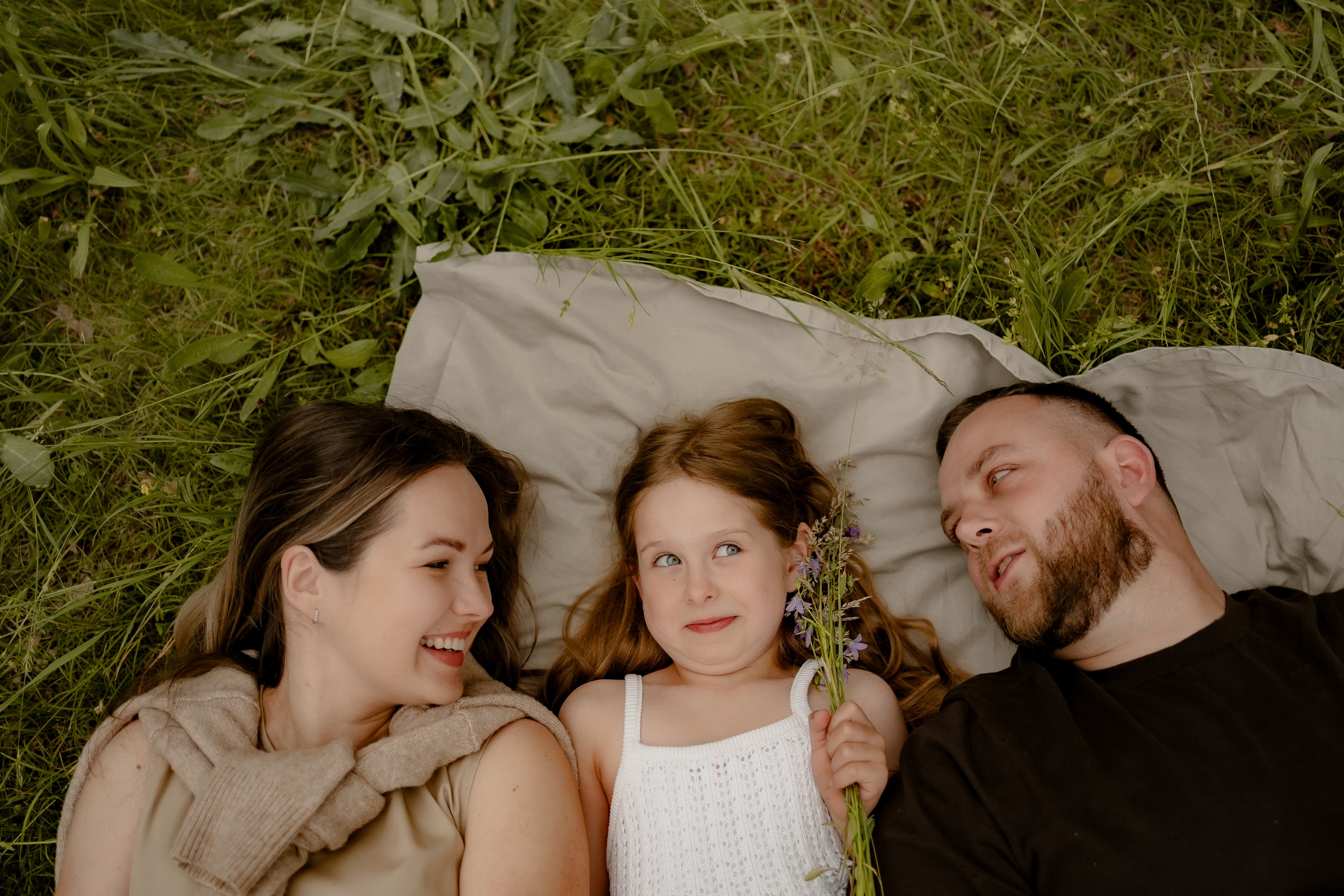 Familie liegt gemeinsam auf einer Decke im Gras und genießt die Zeit miteinander.