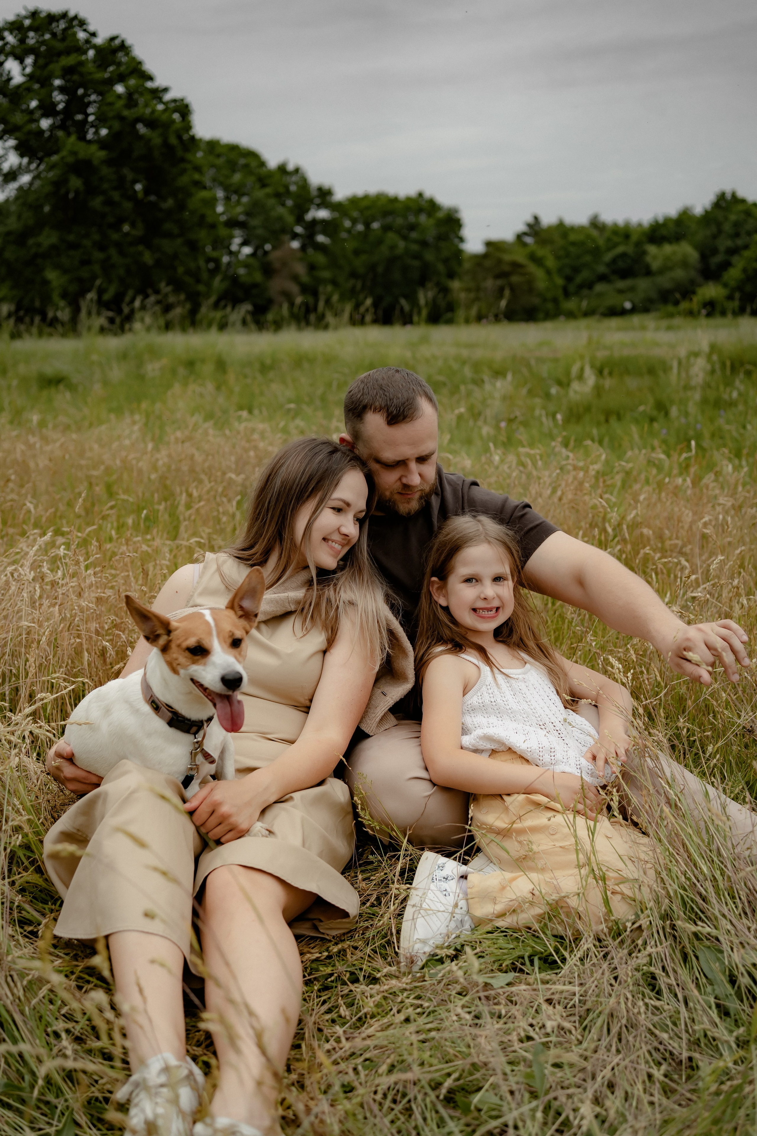 Natürliches Familienportrait von Eltern und Tochter auf einer Decke in der Wiese.