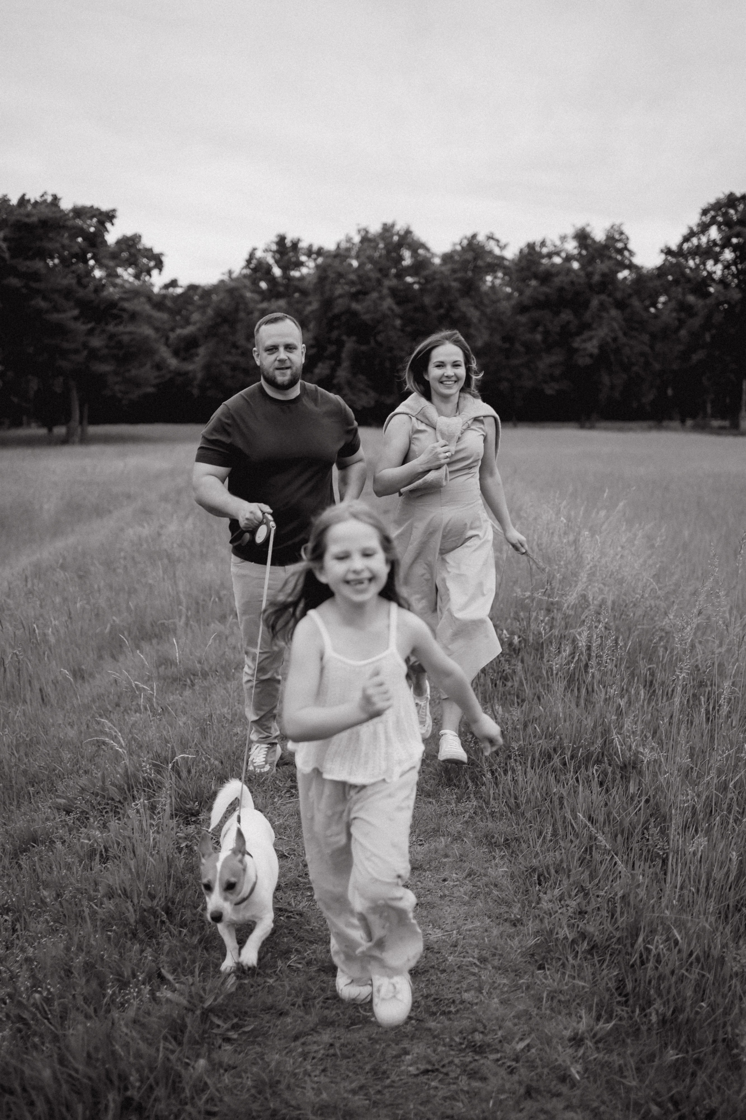 Schwarz-Weiß-Familienfoto von Eltern und Tochter mit Hund auf einer Wiese.