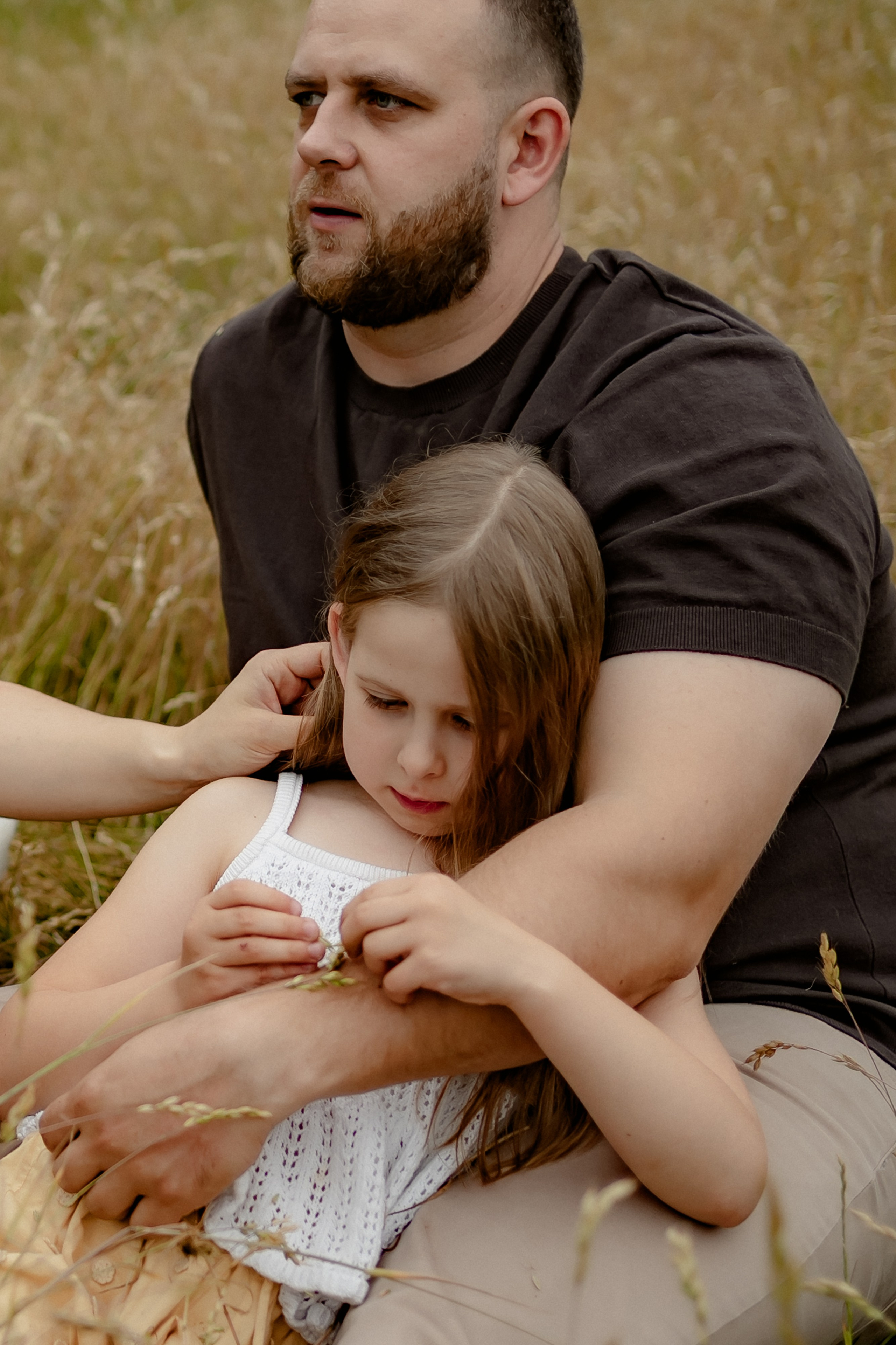 Vater sitzt mit seiner Tochter im Gras und hält sie liebevoll im Arm.