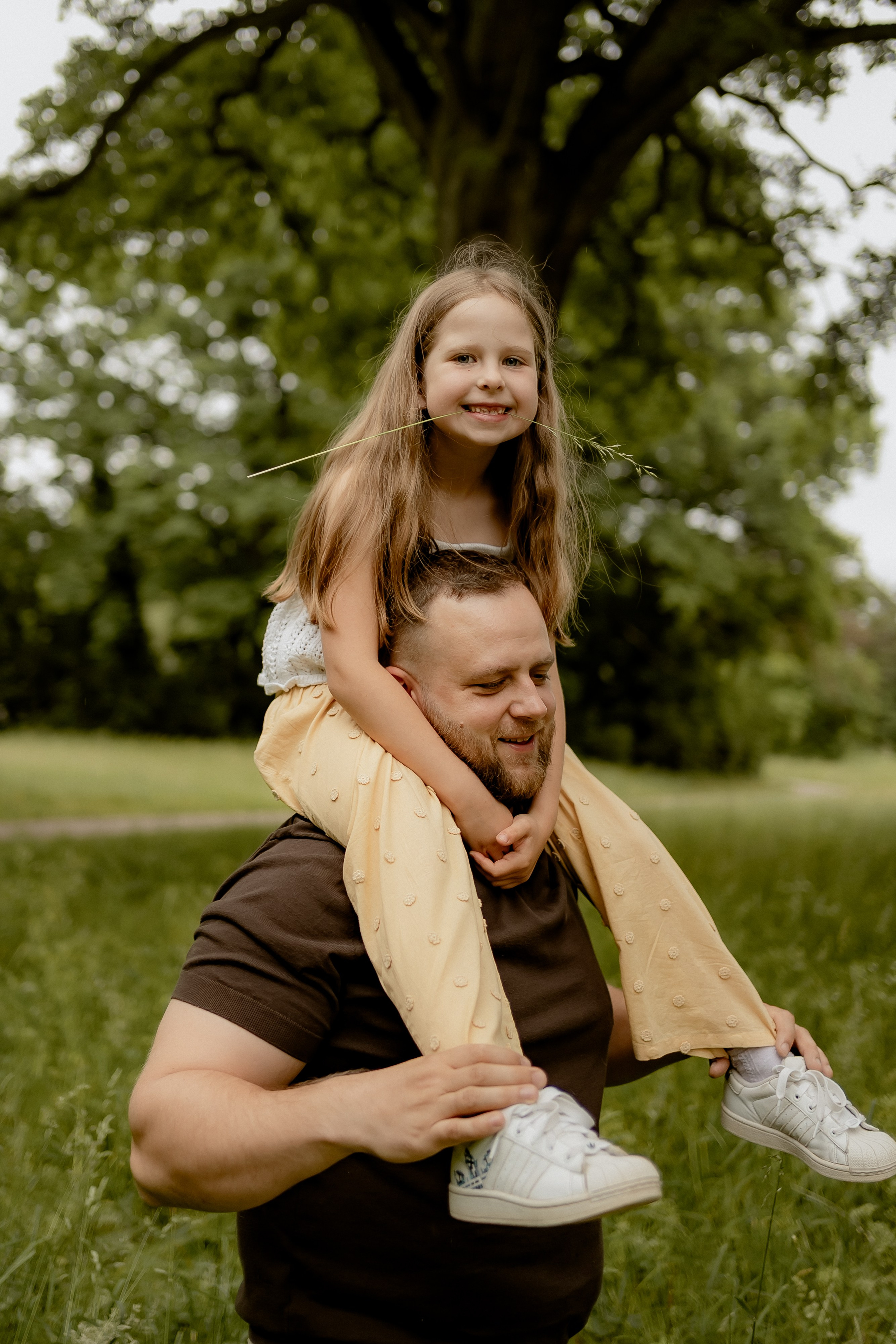 Vater trägt seine Tochter auf den Schultern beim Familienshooting im Grünen.