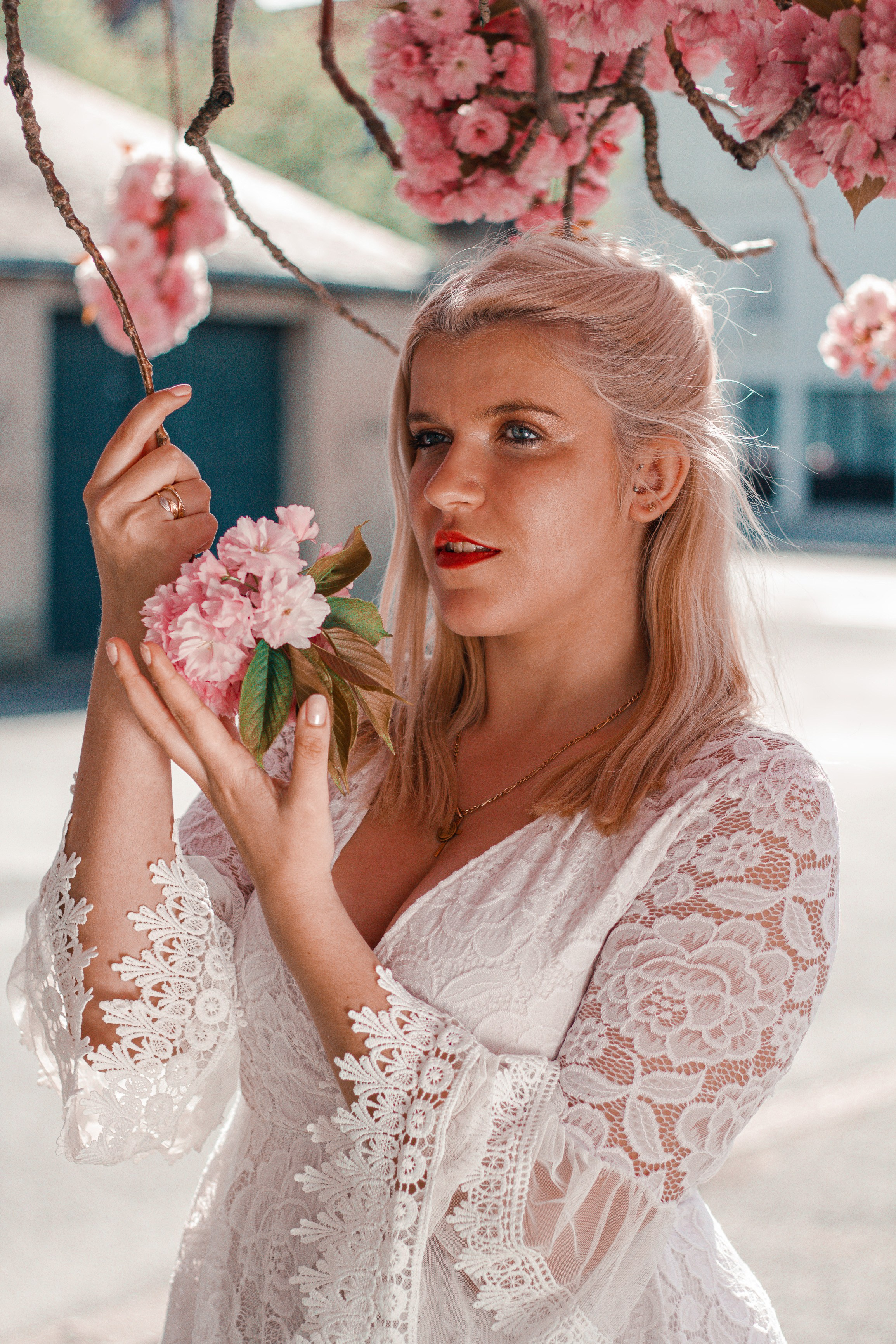 Une femme blonde, habillée en blanc, à côté d'un arbre fleuri