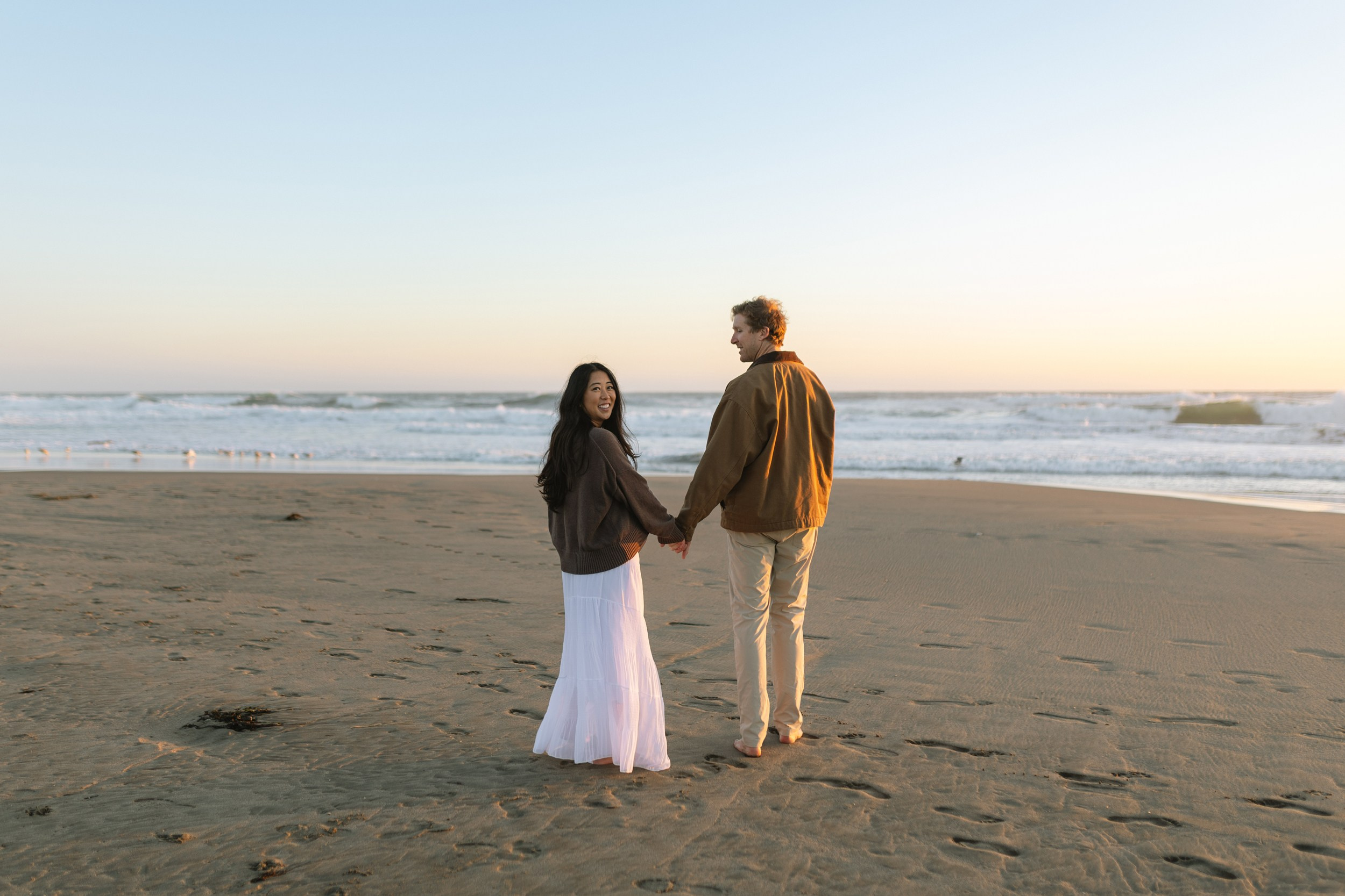 Maternity couple walking along Ocean Beach at sunset in San Francisco
