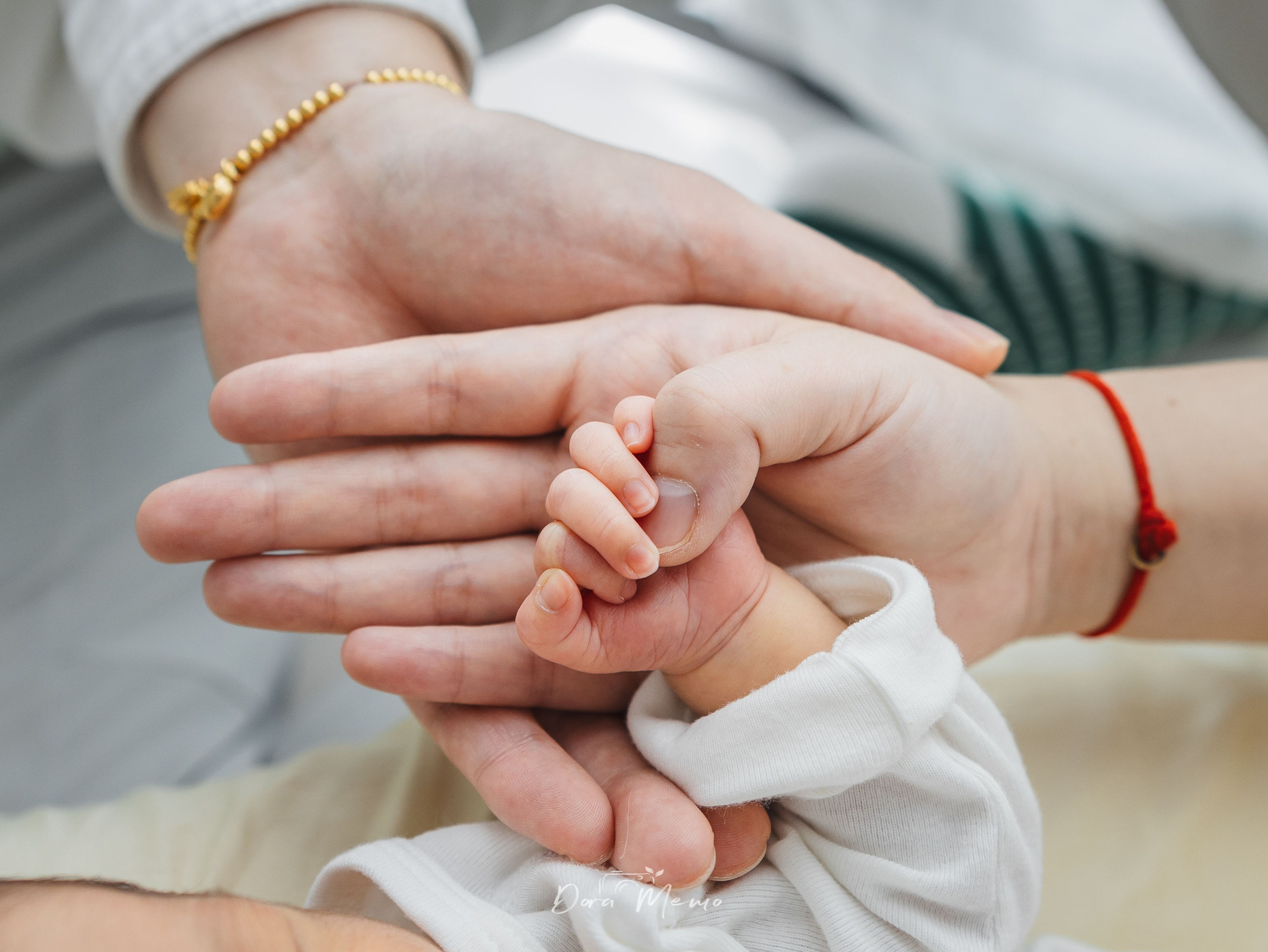 Two adult hands cradling a newborn's tiny hand, symbolizing family bonds and generational love