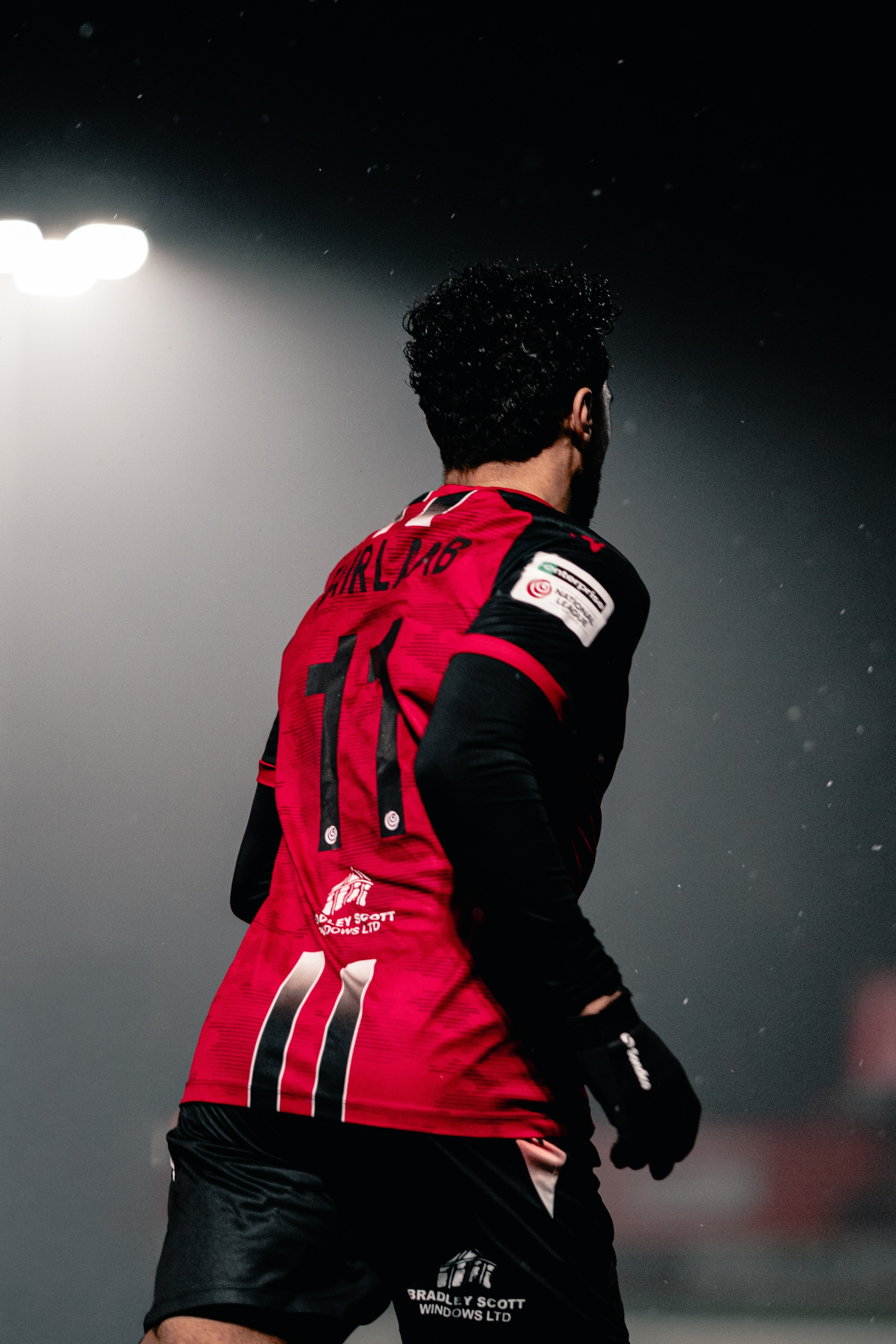 Football player walking off under stadium lights during a night match, atmospheric football photography.