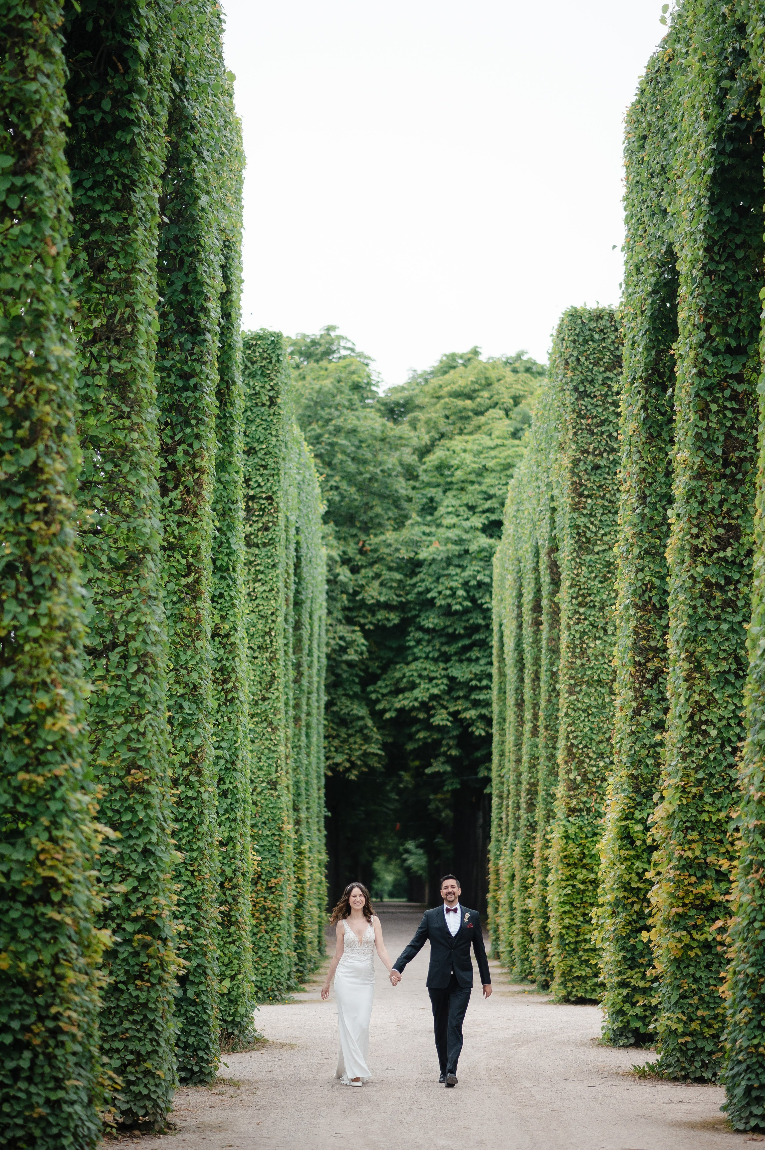Hochzeitspaar beim Spaziergang durch den Park mit hohen grünen Hecken