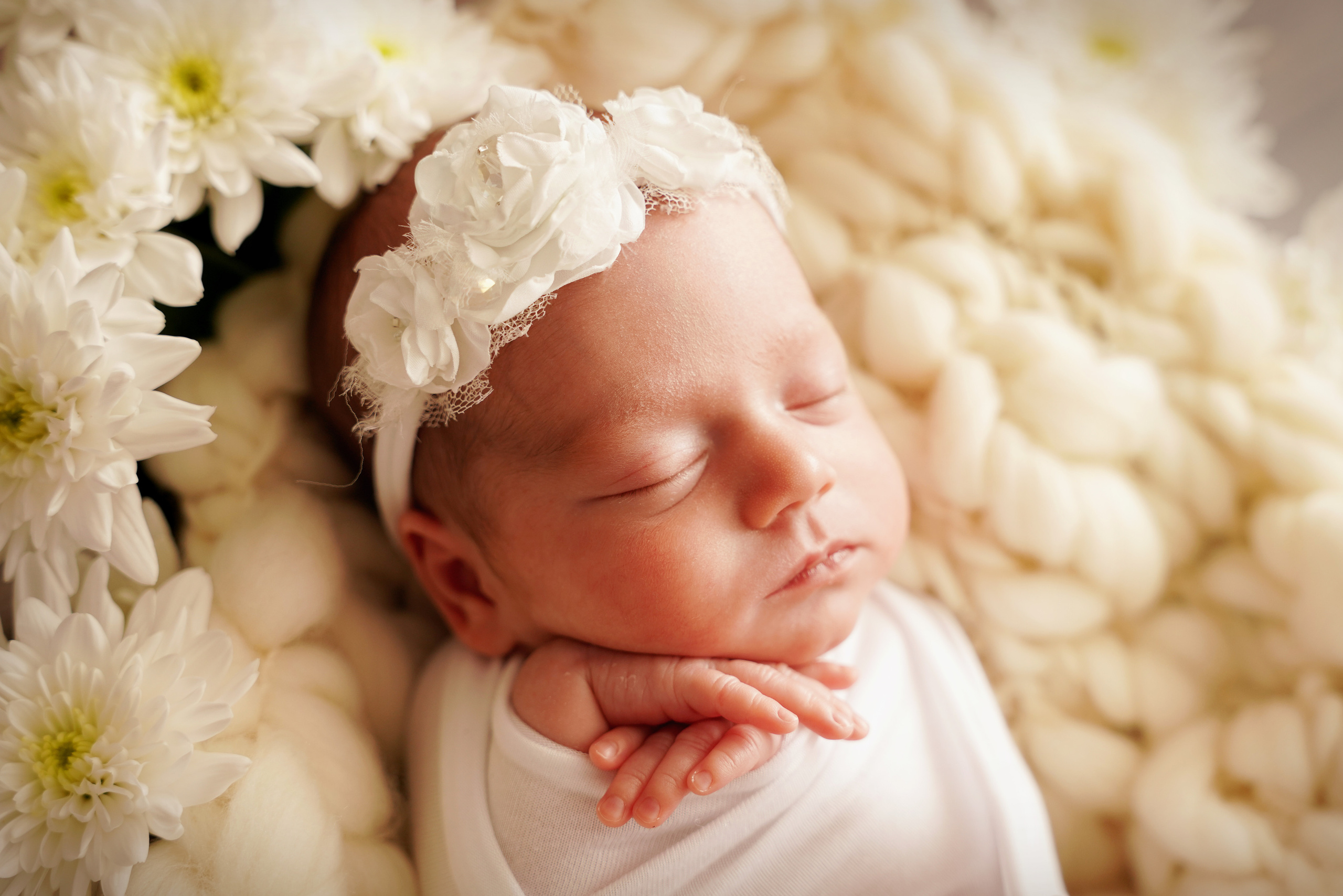 Baby mit den Händen unter dem Kinn liegt in Blumen