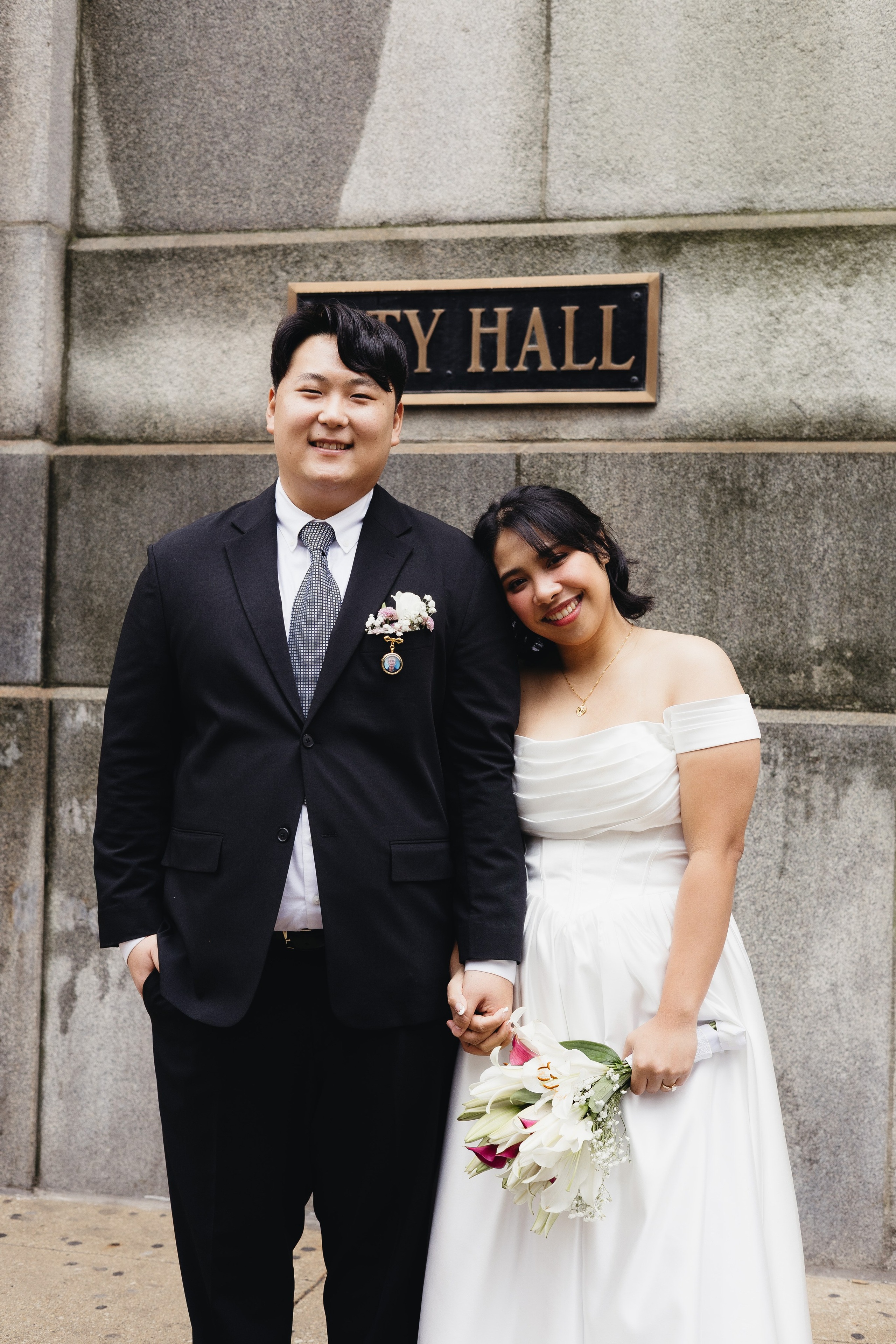 Portrait of the couple smiling in front of the City Hall sign