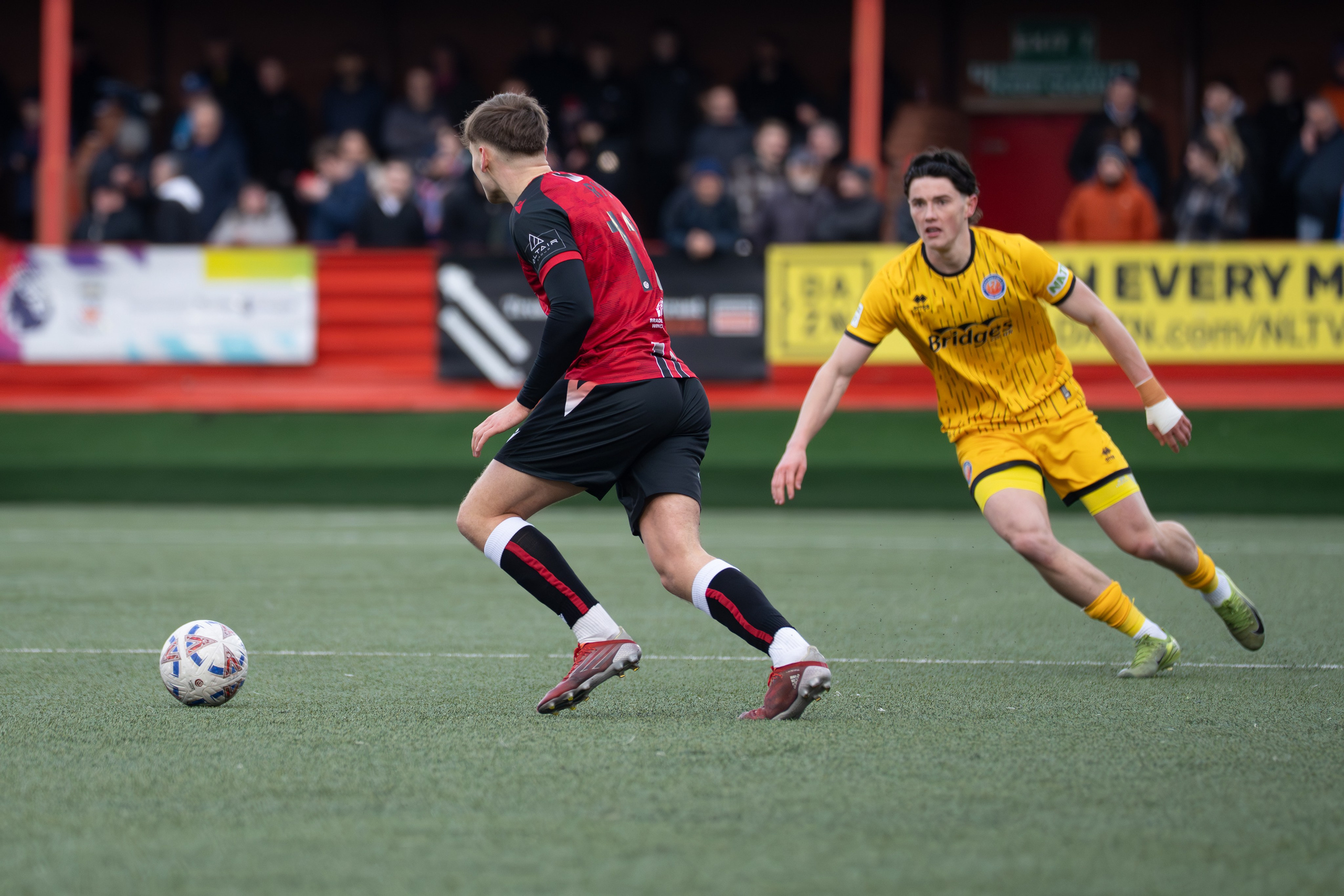 Tamworth, England — February 14, 2026: Tamworth’s Joe Rye carries the ball under pressure from an Aldershot Town player during the Enterprise National League match between Tamworth and Aldershot Town at The Lamb Ground. Photo: Jay Soundo