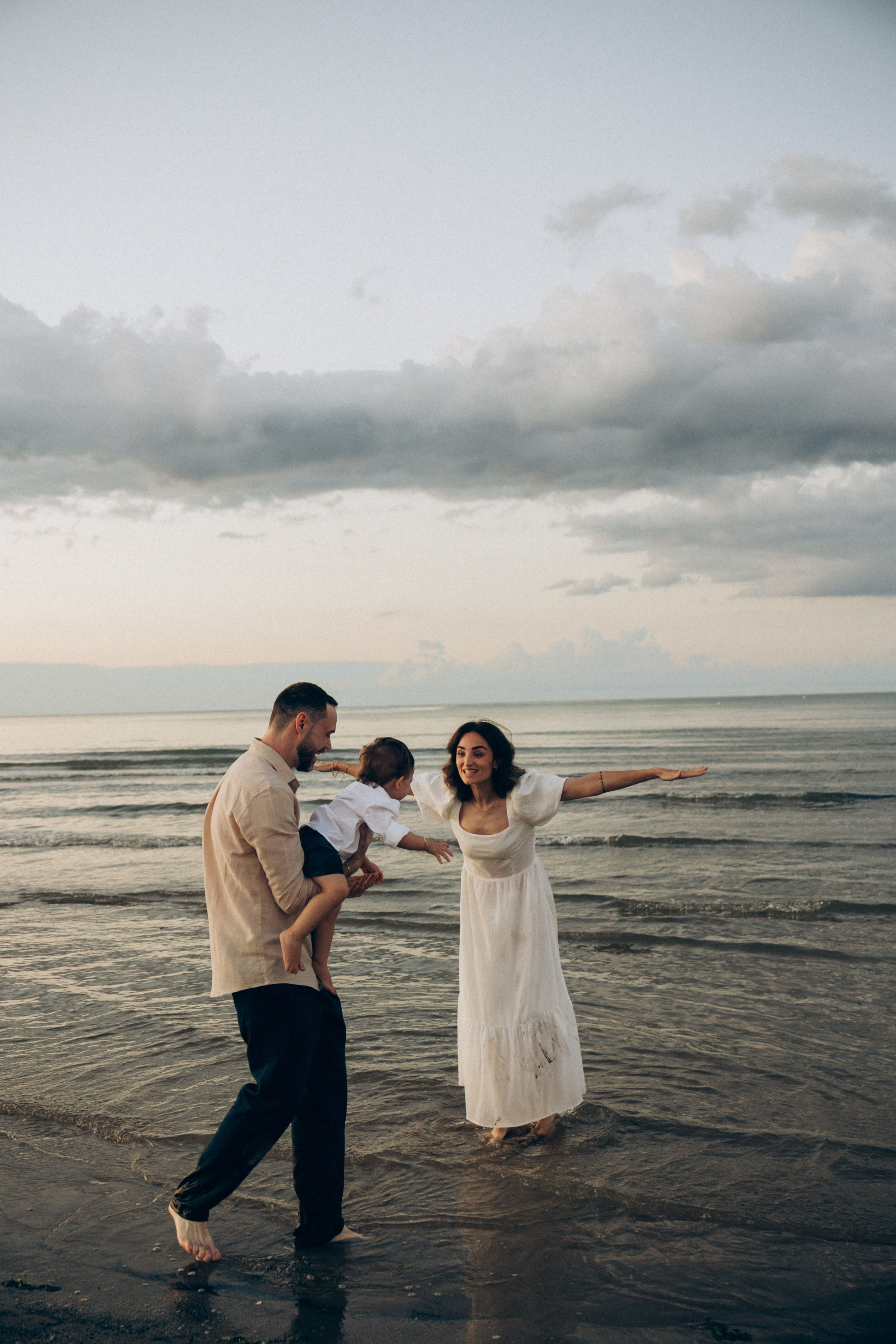 Famiglia che gioca con il bambino sulla spiaggia di Riccione. Momenti spontanei e pieni di vita nella fotografia di famiglia.