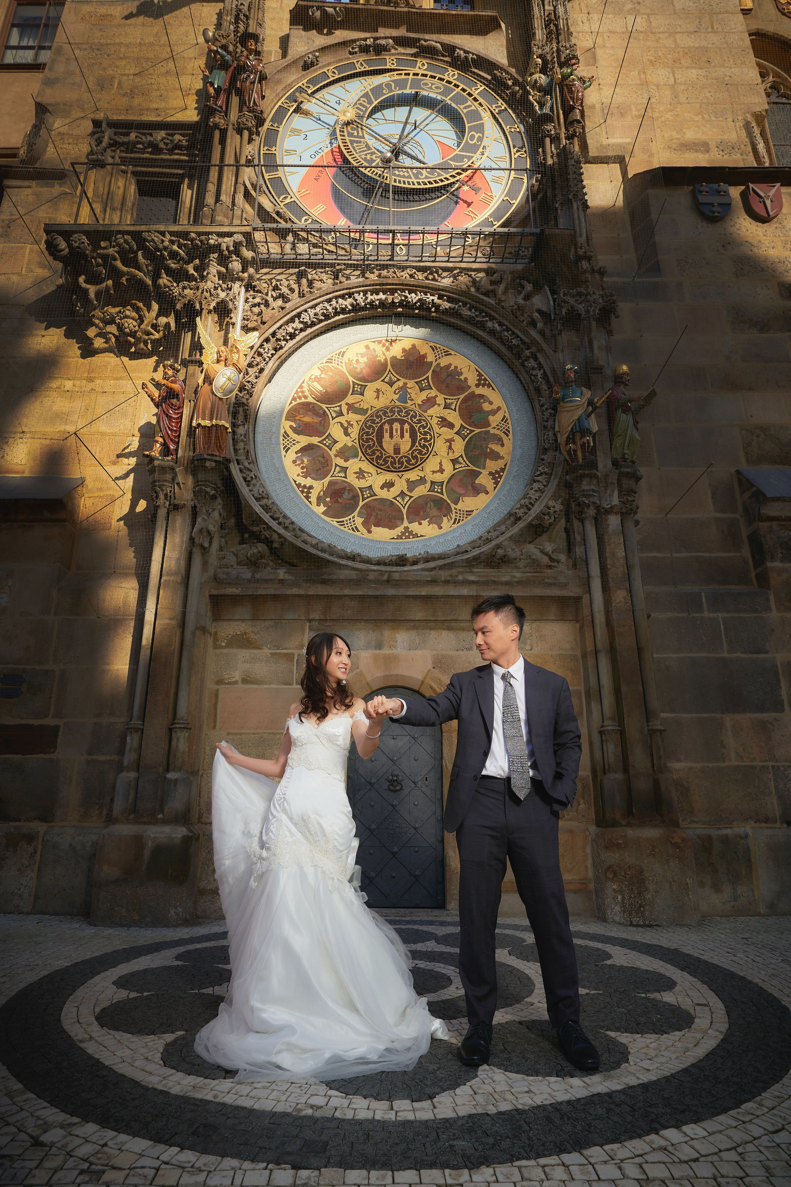 Eva and Conan playfully stand under the Astronomical Clock in the sunlit Old Town Square.