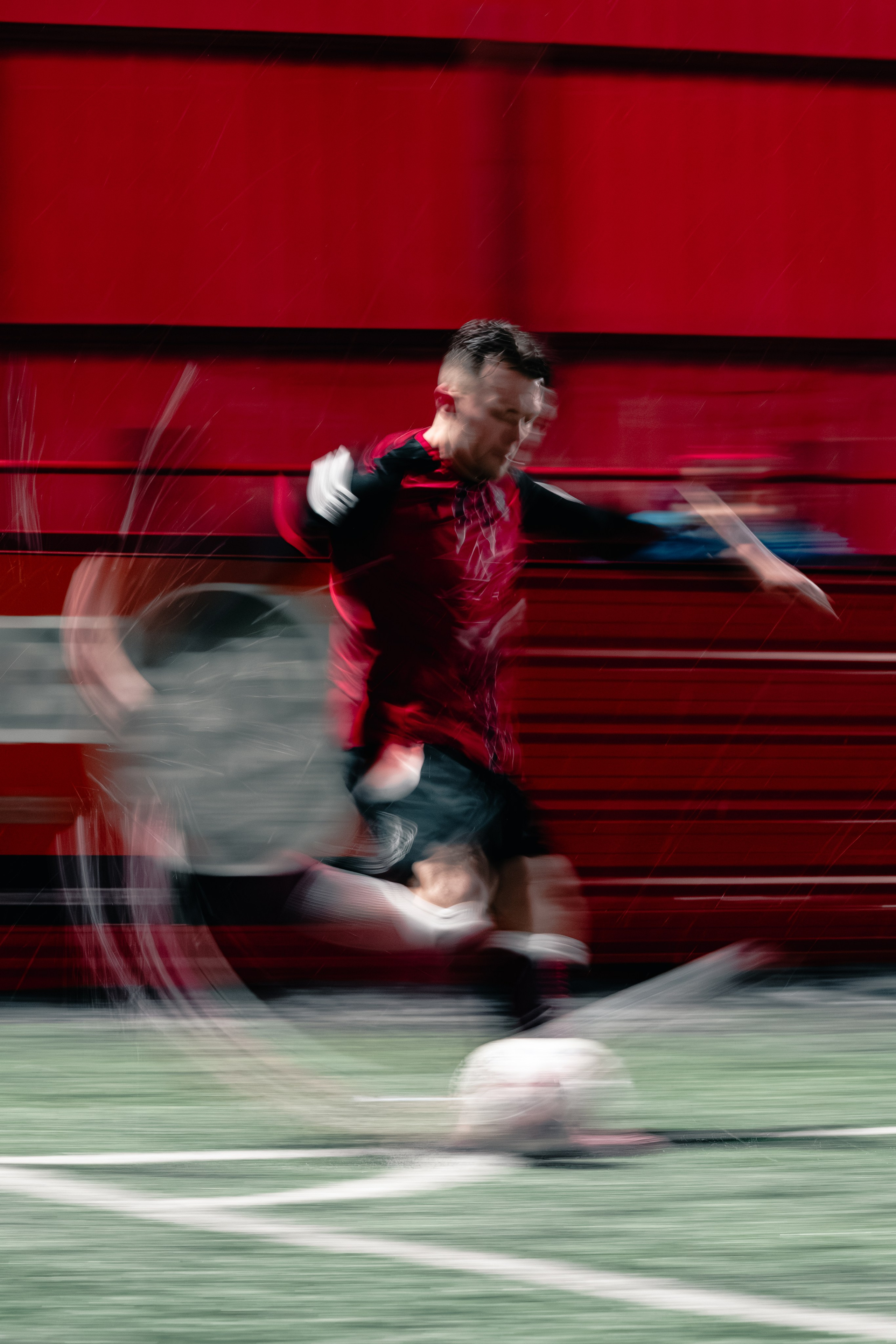 Football player in red kit sprinting with motion blur during a match, dynamic sports action photography.