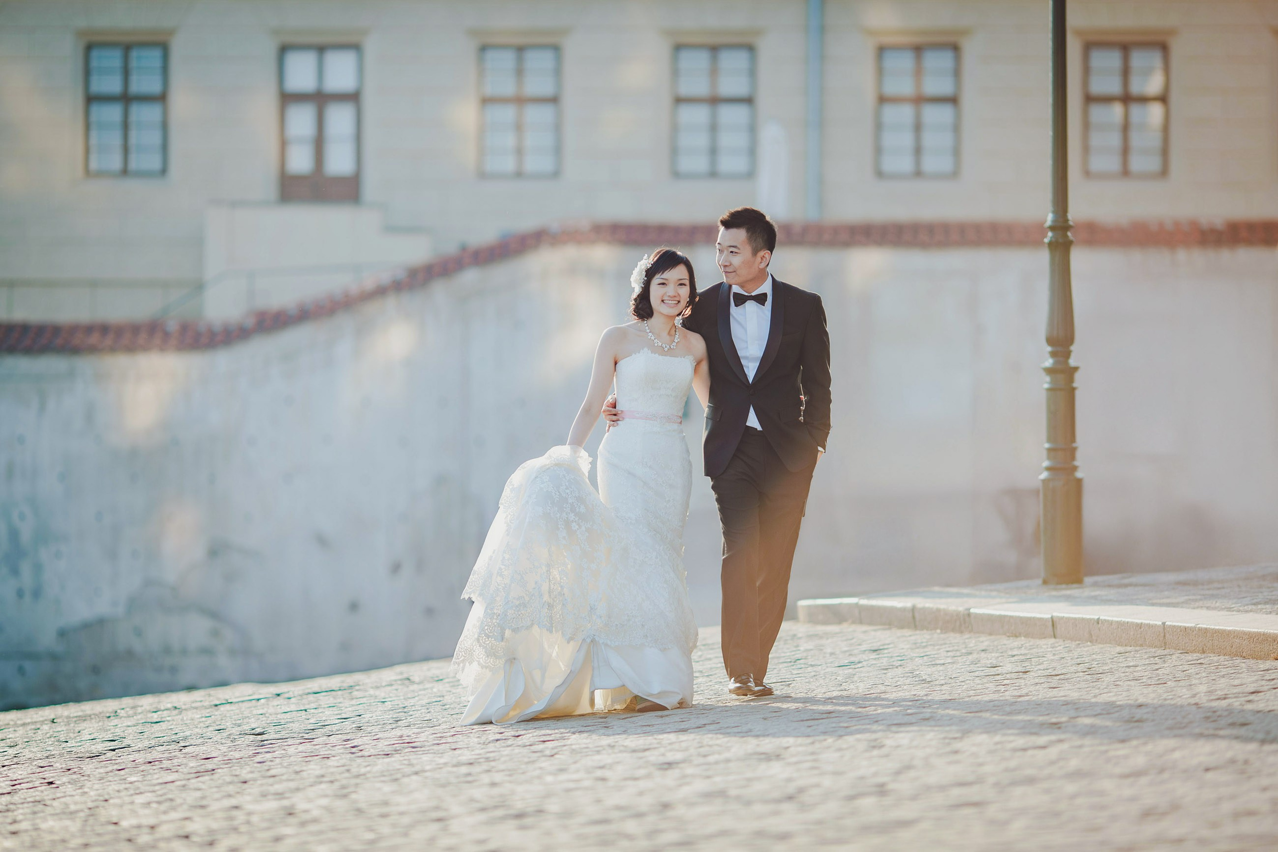 As the sun creates patters of light reflected from the windows above, a Hong Kong couple dressed in their wedding attire walk alone through the courtyards of Prague Castle.