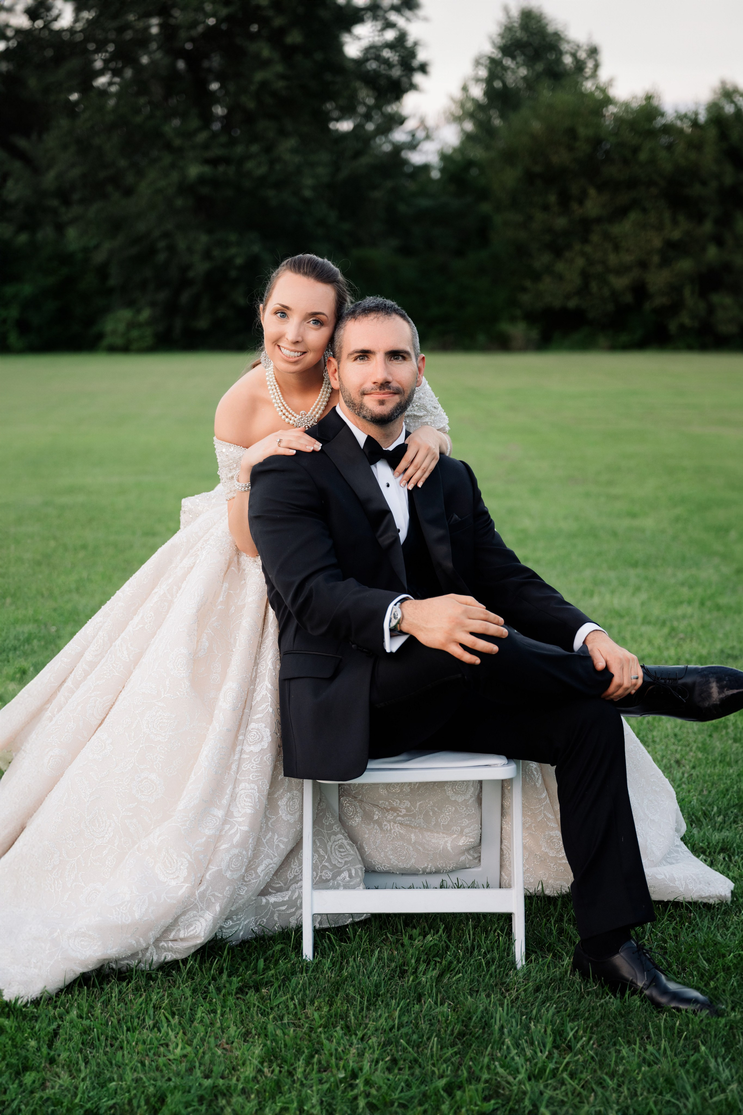 a bride and groom sitting on a chair in a field