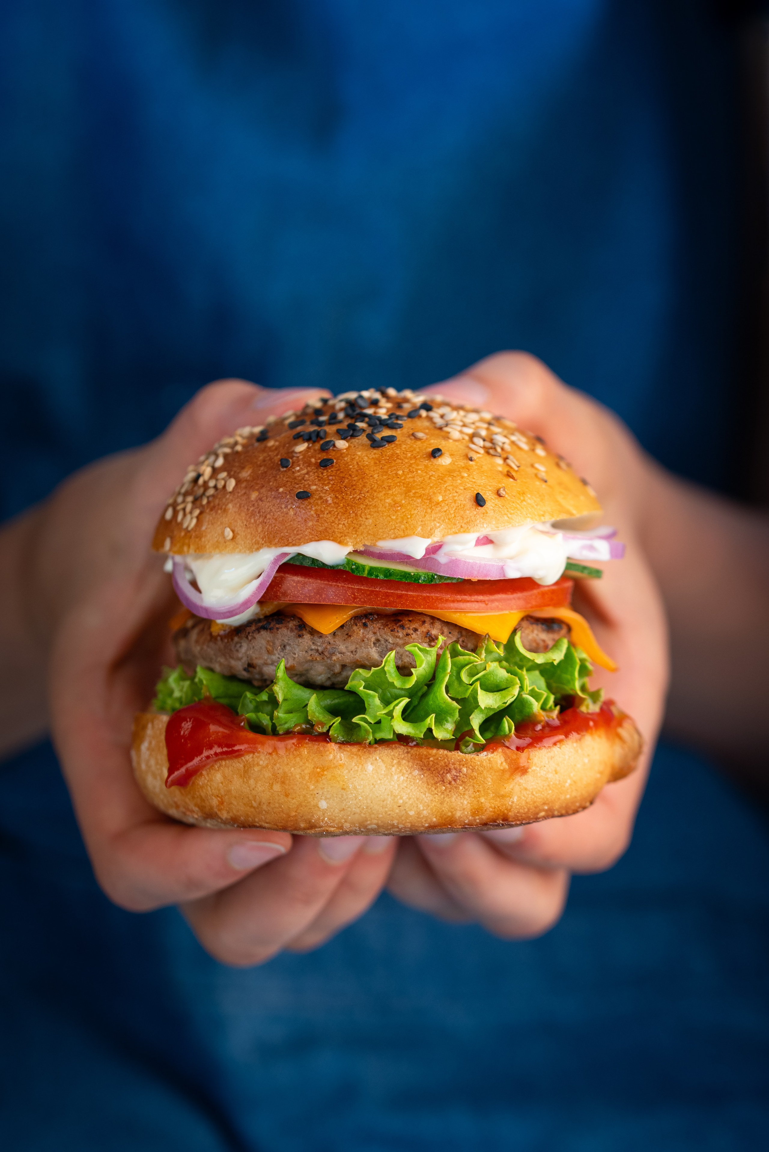 ein saftiger, geschichteter Burger mit Salat, Tomate und Käse in den Händen einer jungen Frau