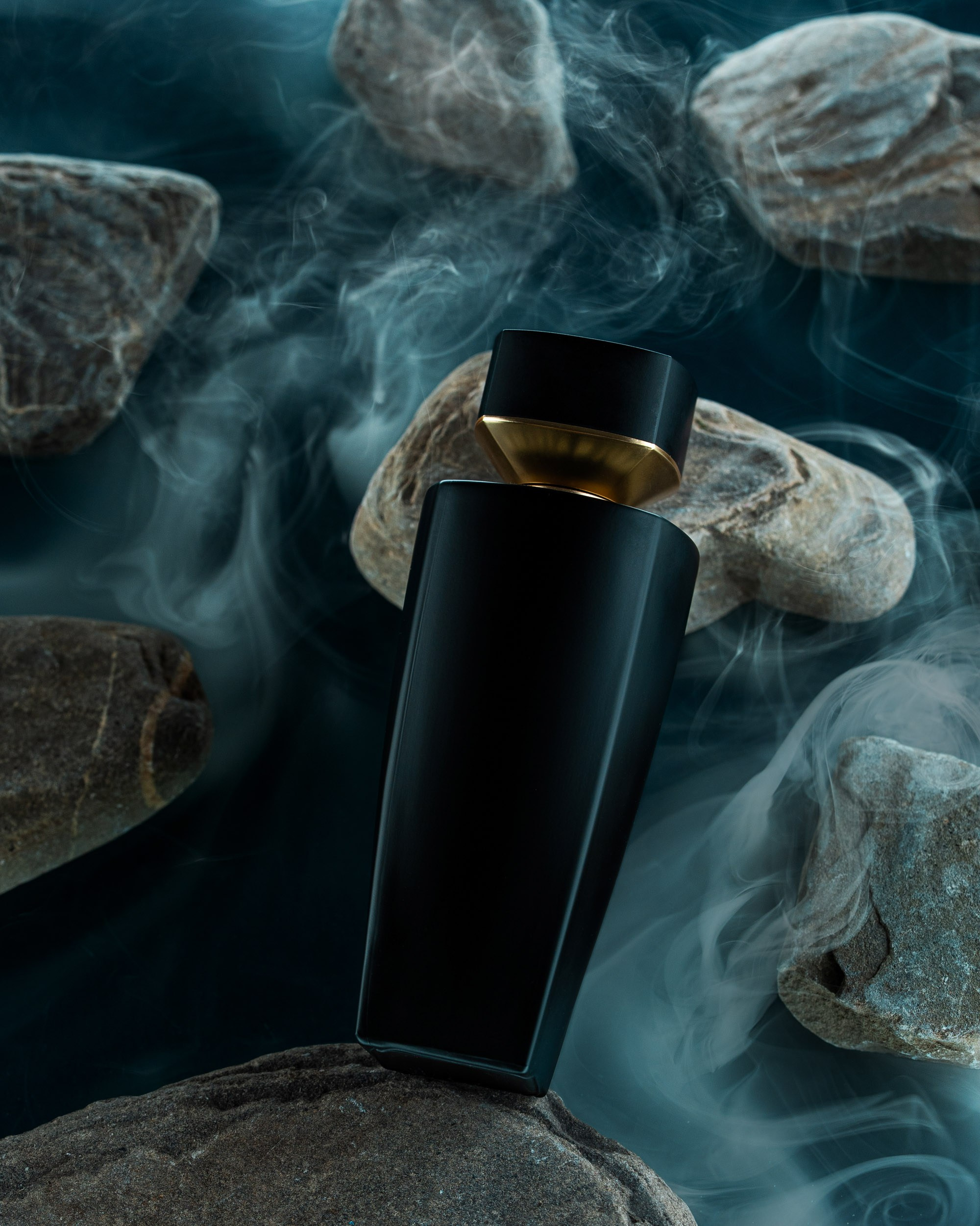 Qara, tünd rəngli ətir butulkası tünd fonda, ətrafı dumanlı tüstü ilə əhatə olunmuş qayalar və daşlar arasında dramatik şəkildə təqdim olunur.