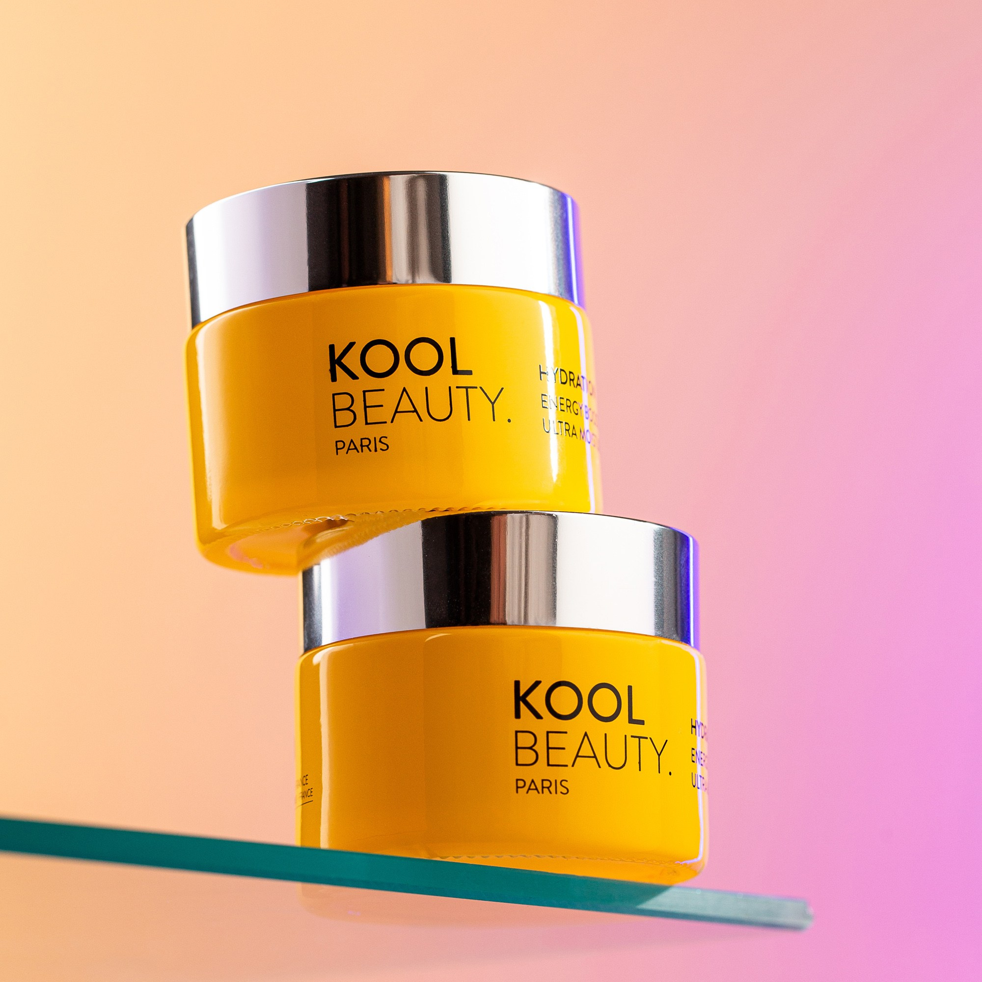 Stacked KOOL Beauty cream jars on glass shelf with pastel gradient background, product photography
