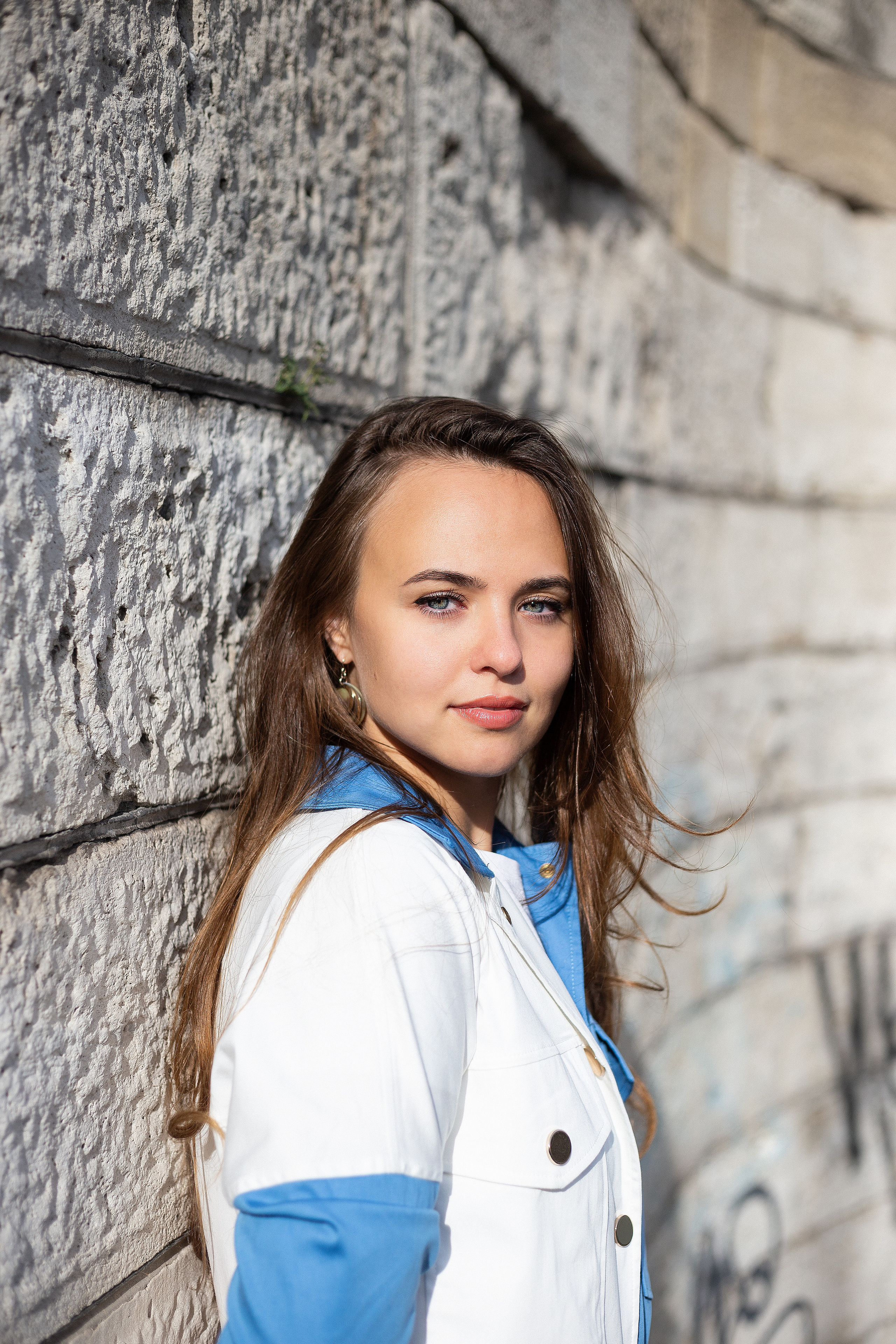 Photo a girl in a white and blue jacket against the wall