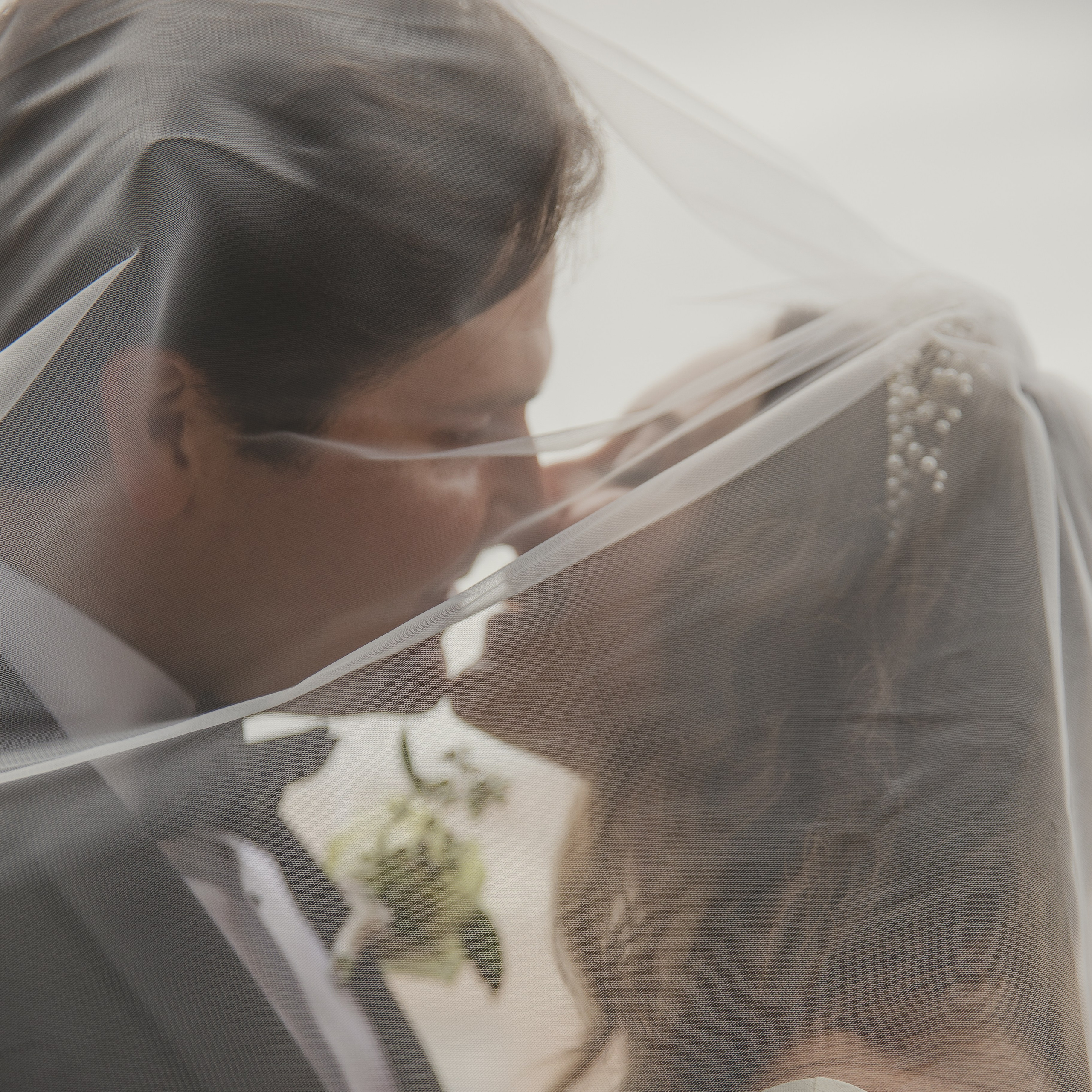A newly married couple sharing a kiss under a romantic veil in a picturesque garden.