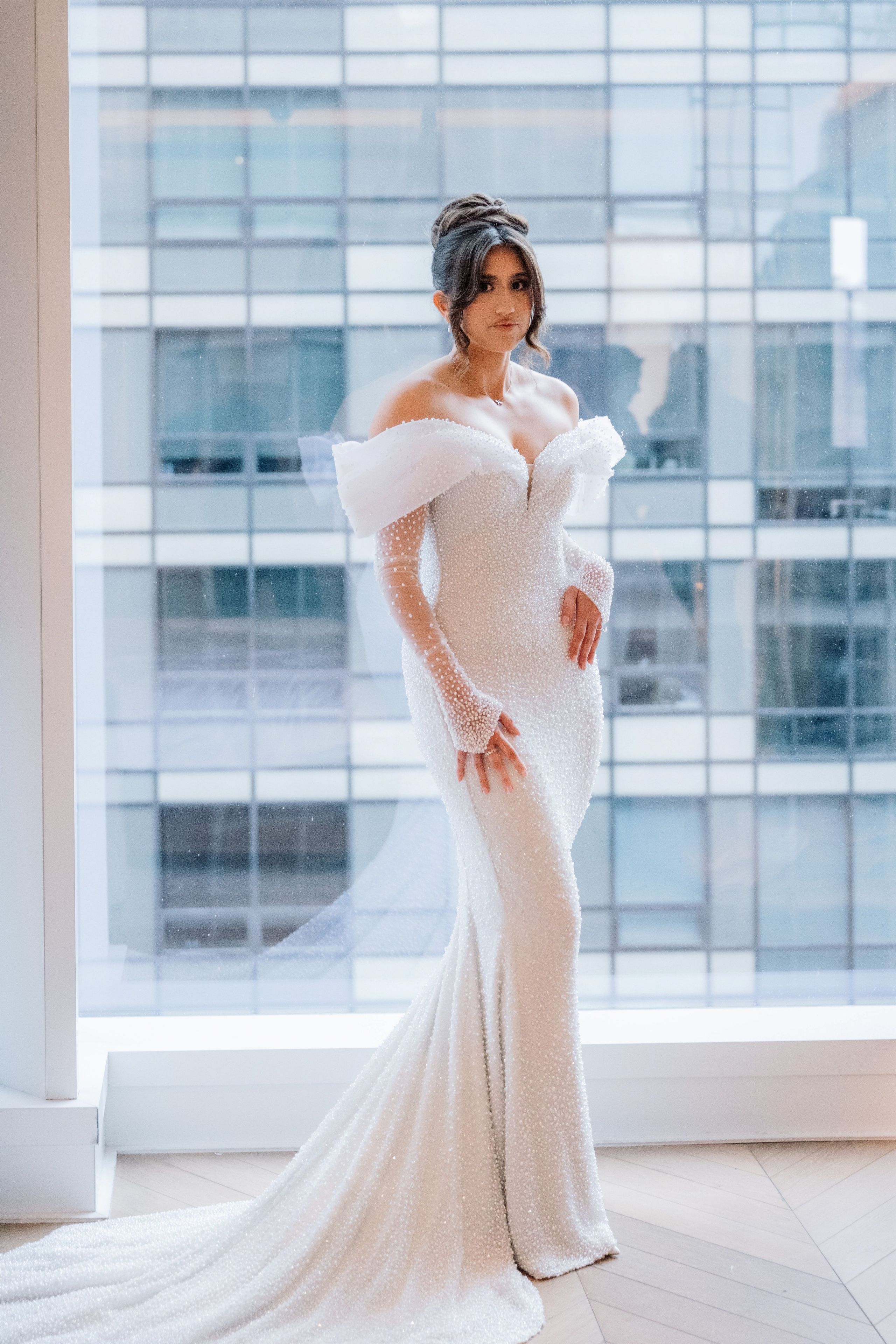 a bride in a white gown standing in front of a window