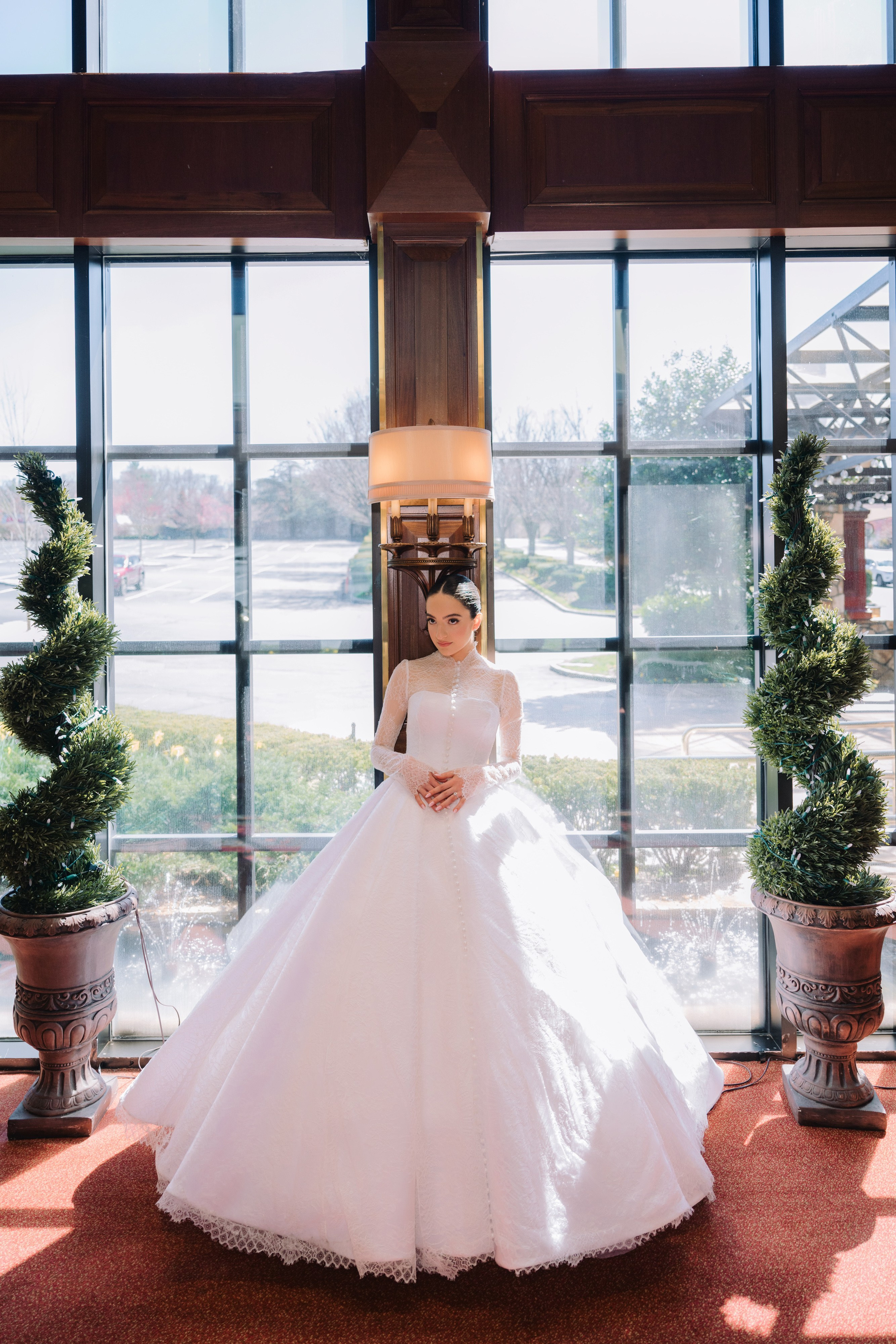 a bride in a white wedding dress standing in front of a large window