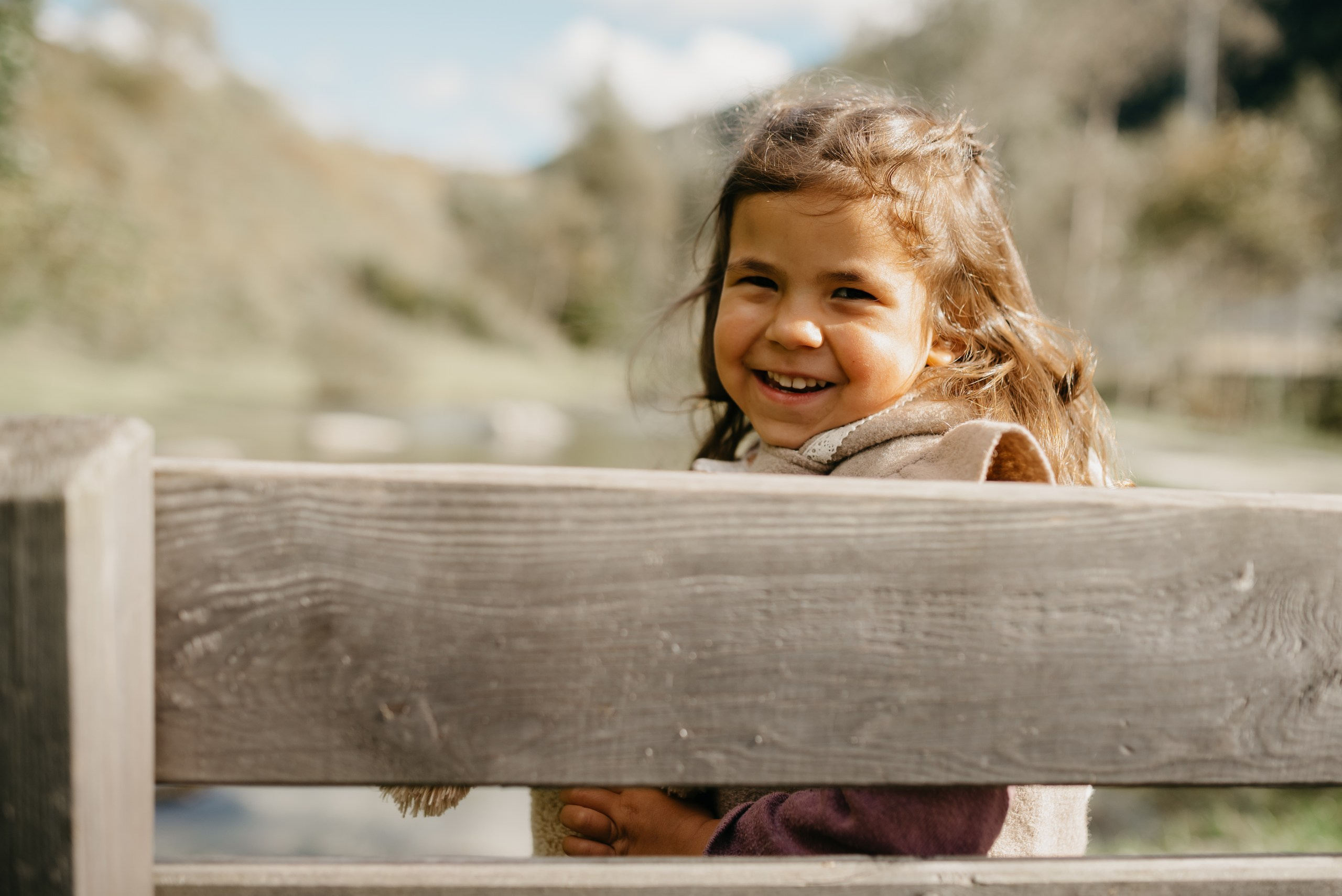 ein Mädchen sitzt auf einer Bank mit einer bergigen Landschaft im Hintergrund