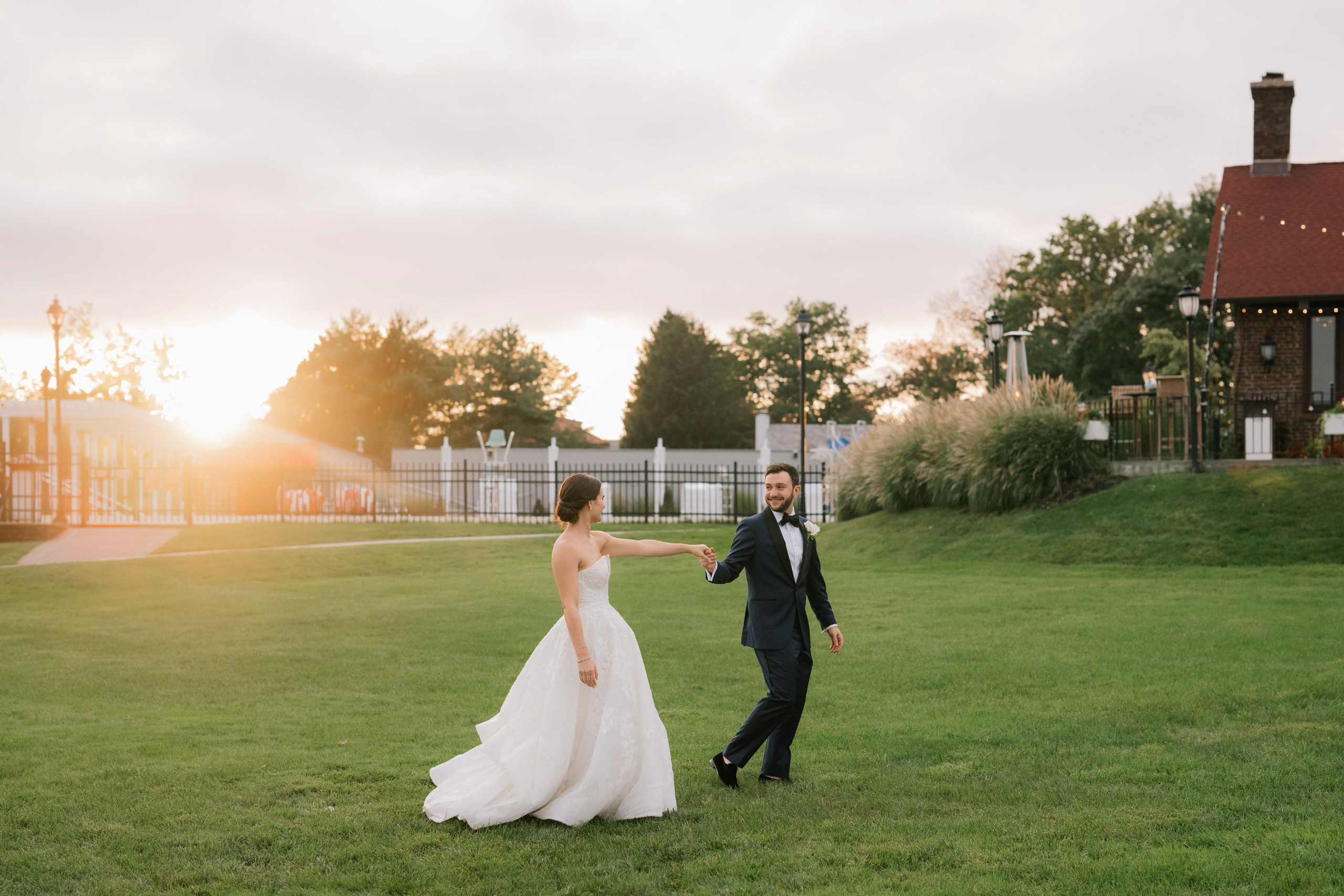 a bride and groom walking through the grass at sunset