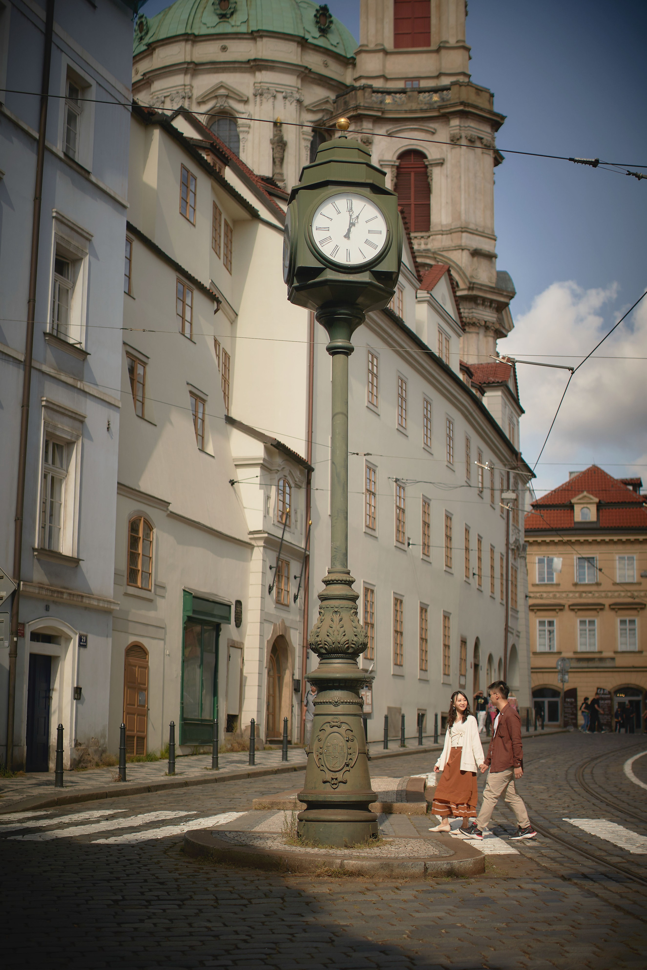 Newlyweds crossing the street under the clock with St. Nicholas Church above in Malá Strana.