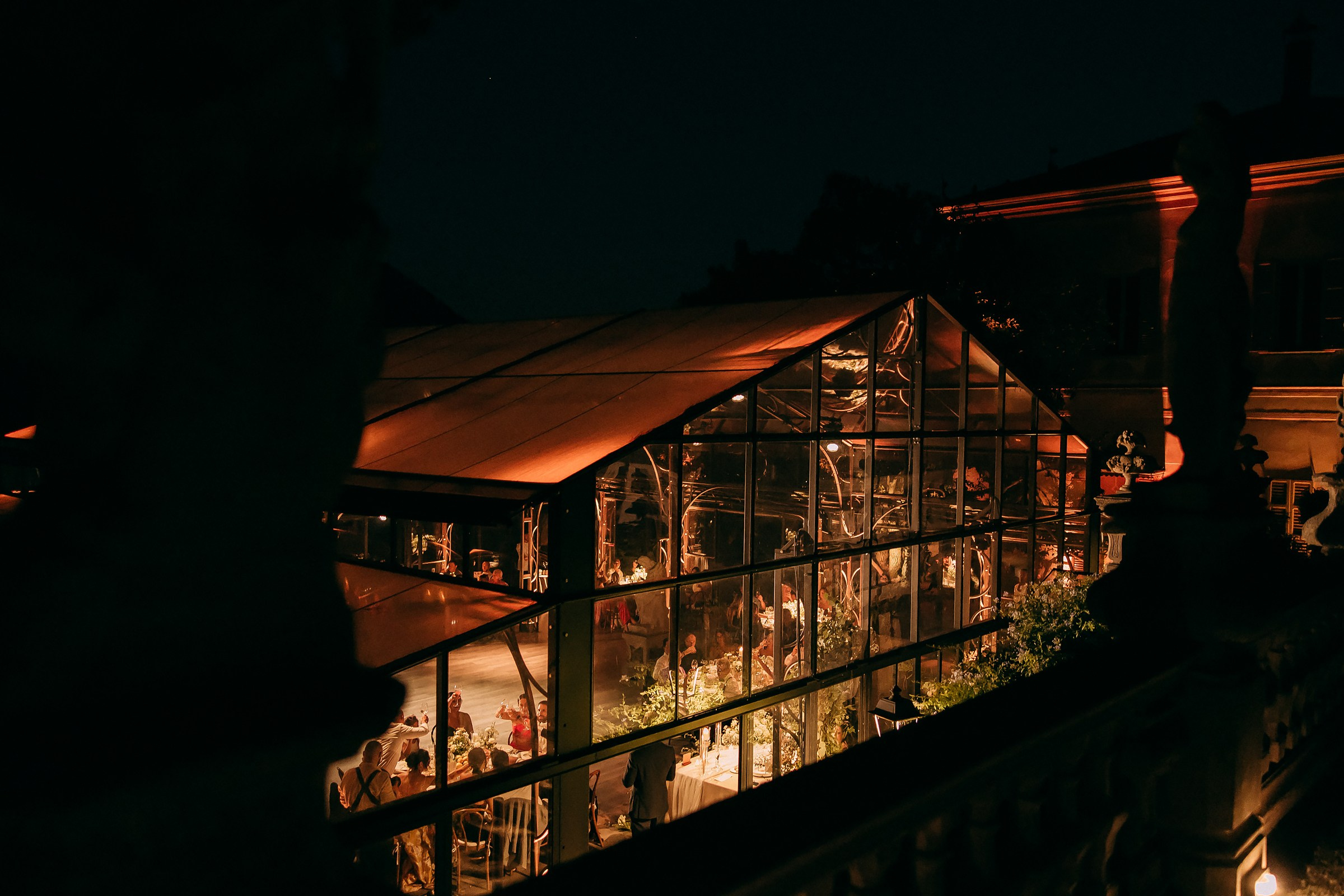 Stunning glass pavilion of Villa Pizzo illuminated at night, hosting an elegant wedding celebration.
