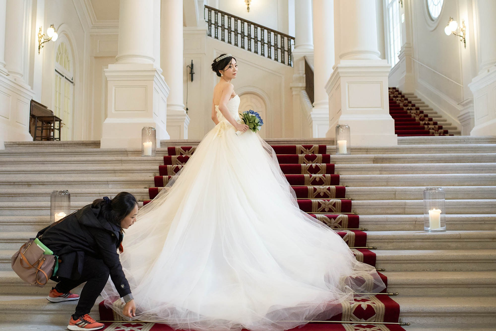 The hair and makeup artist adjusts the bride's dress for a few formal portraits.