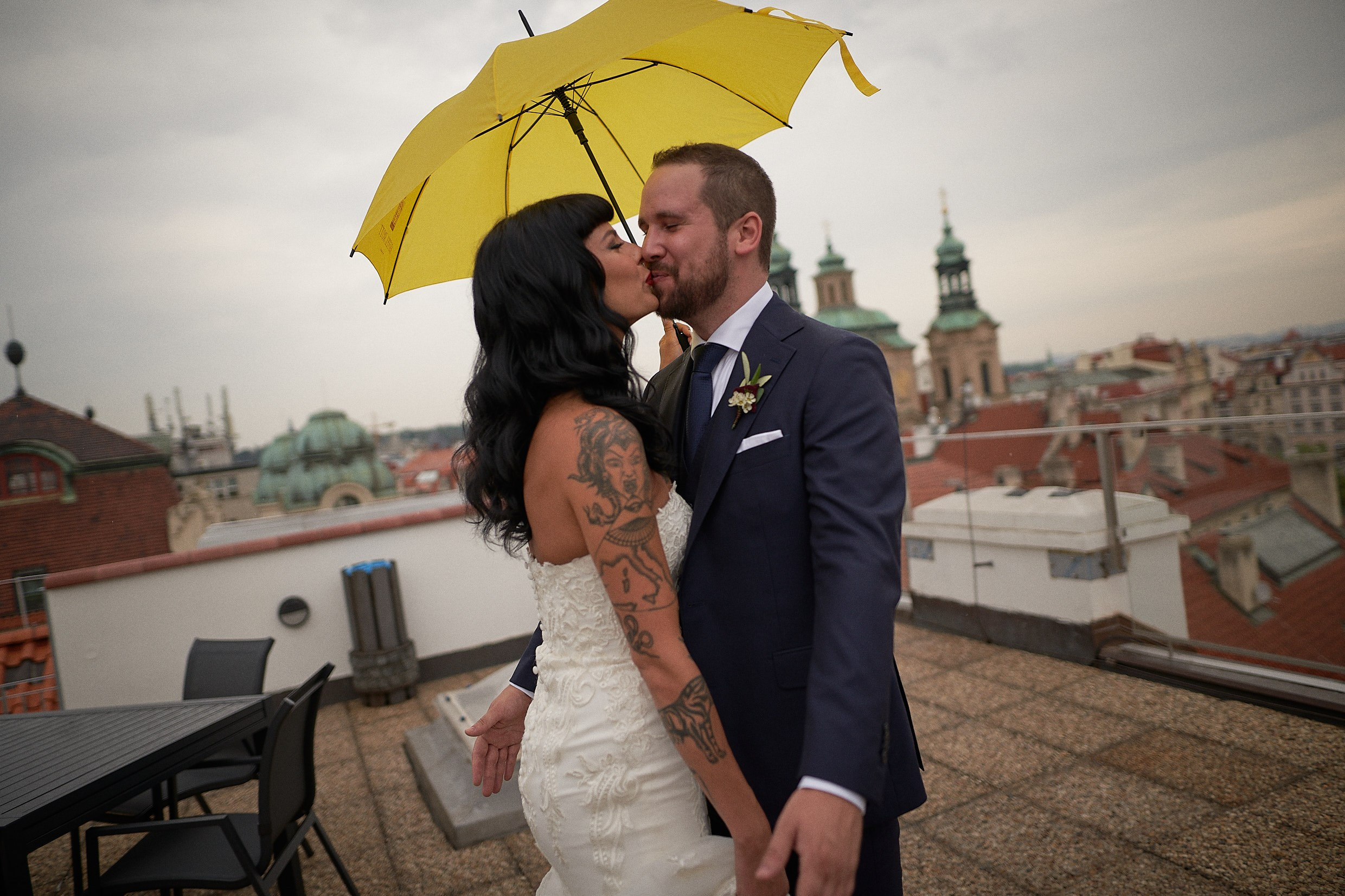 Newly-revealed couple kissing with dramatic Prague skyline backdrop.