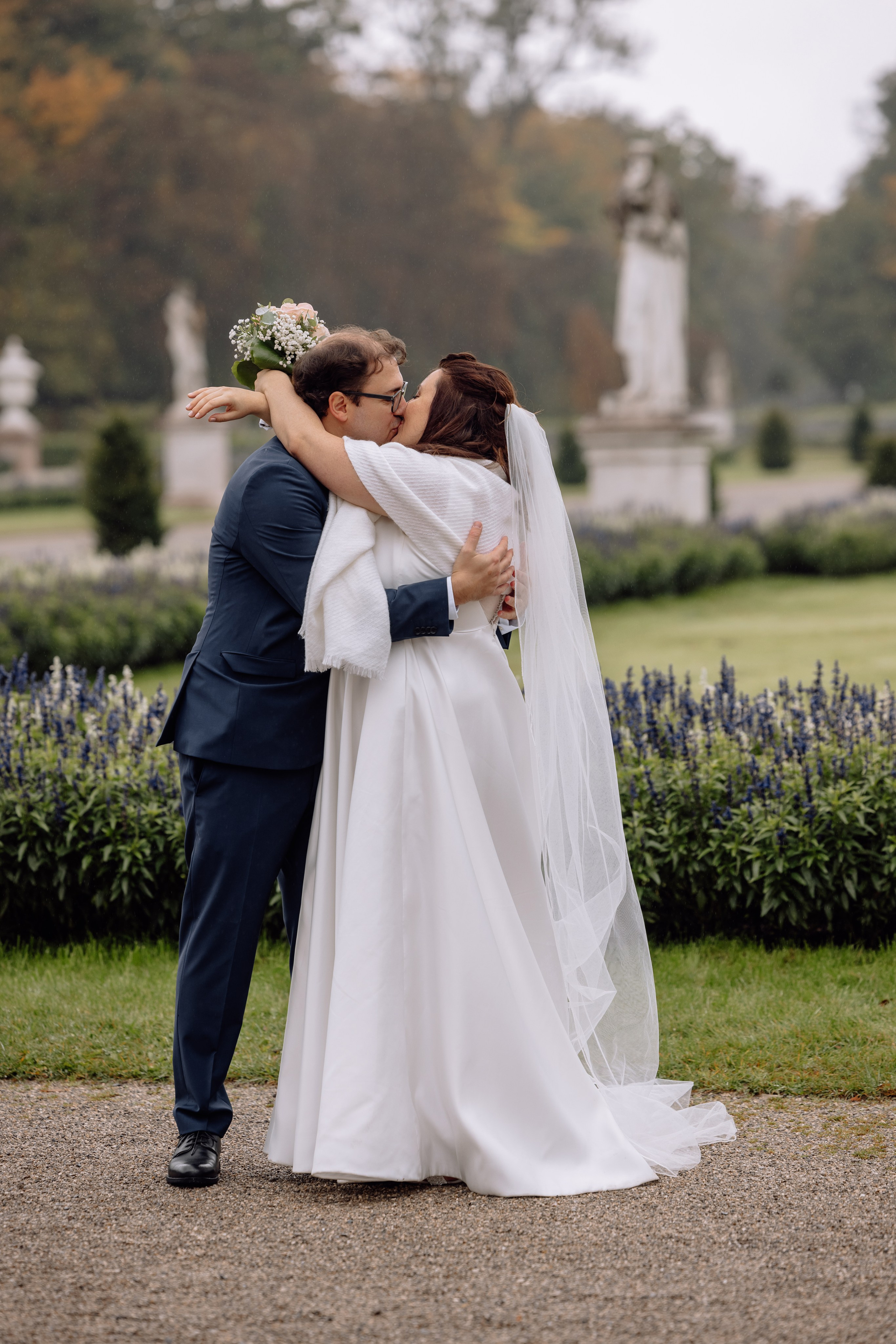 Paar umarmt sich im Regen auf Hochzeitsfotos vor dem Schloss Nymphenburg