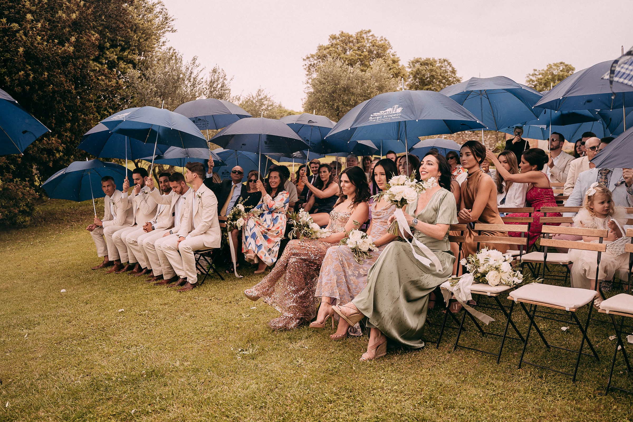 Guests elegantly seated under blue umbrellas, enjoying the outdoor wedding despite the light drizzle.