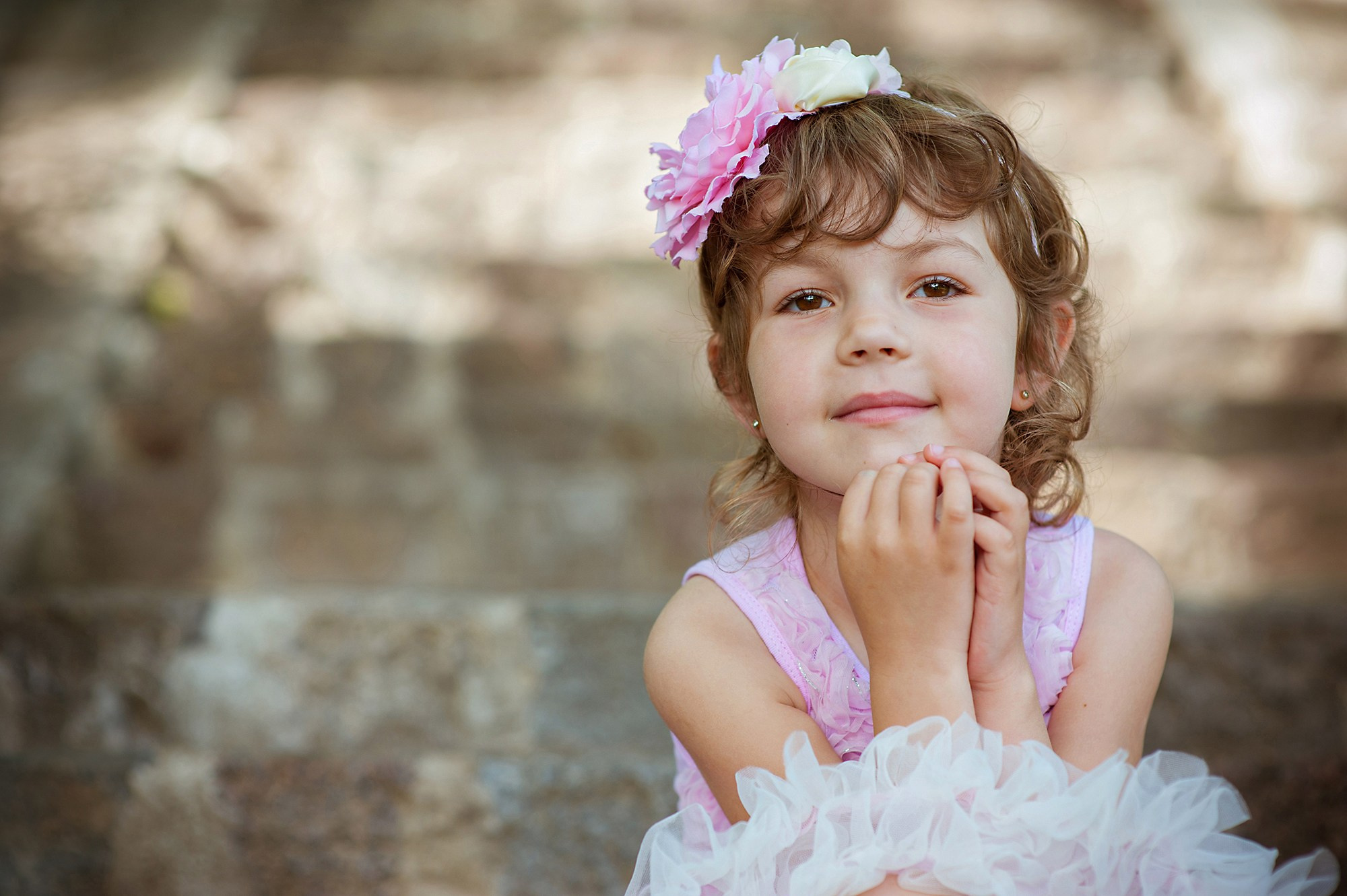 A cute little girl with a bow on her head sits on the stairs in the park, family photographer Riga