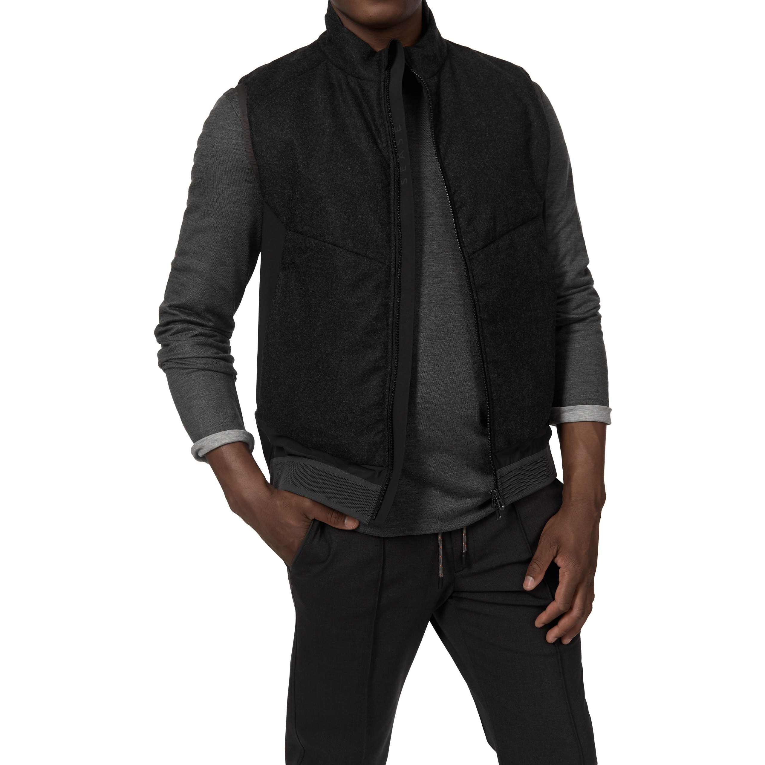 Model in schwarzer Jacke mit grauem Pullover, Hände in Taschen, Studioaufnahme.