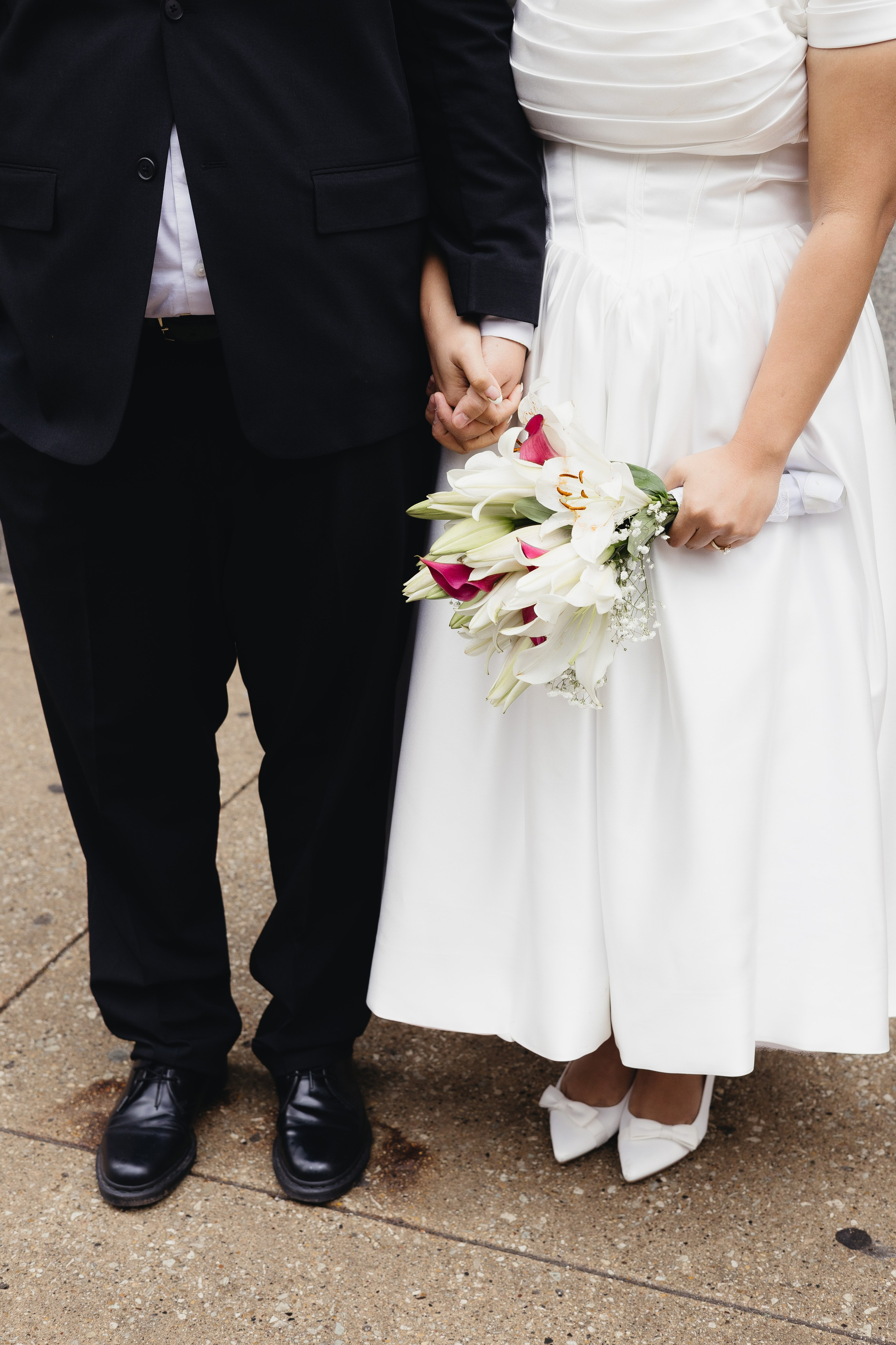 Detail photo of couple holding hands, wedding shoes and bouquet visible