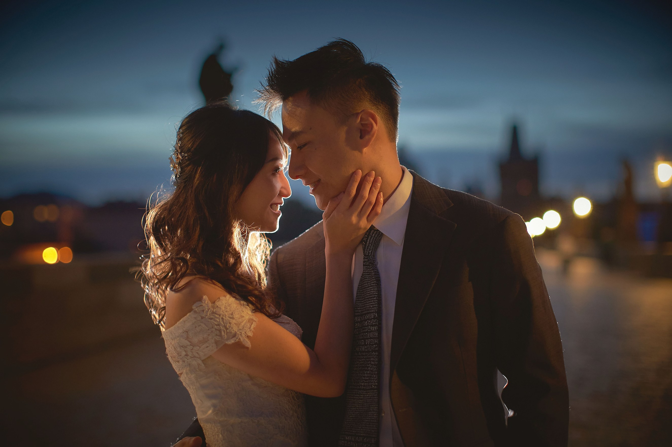 Close-up tender embrace of newlyweds Eva and Conan on Charles Bridge at dawn.