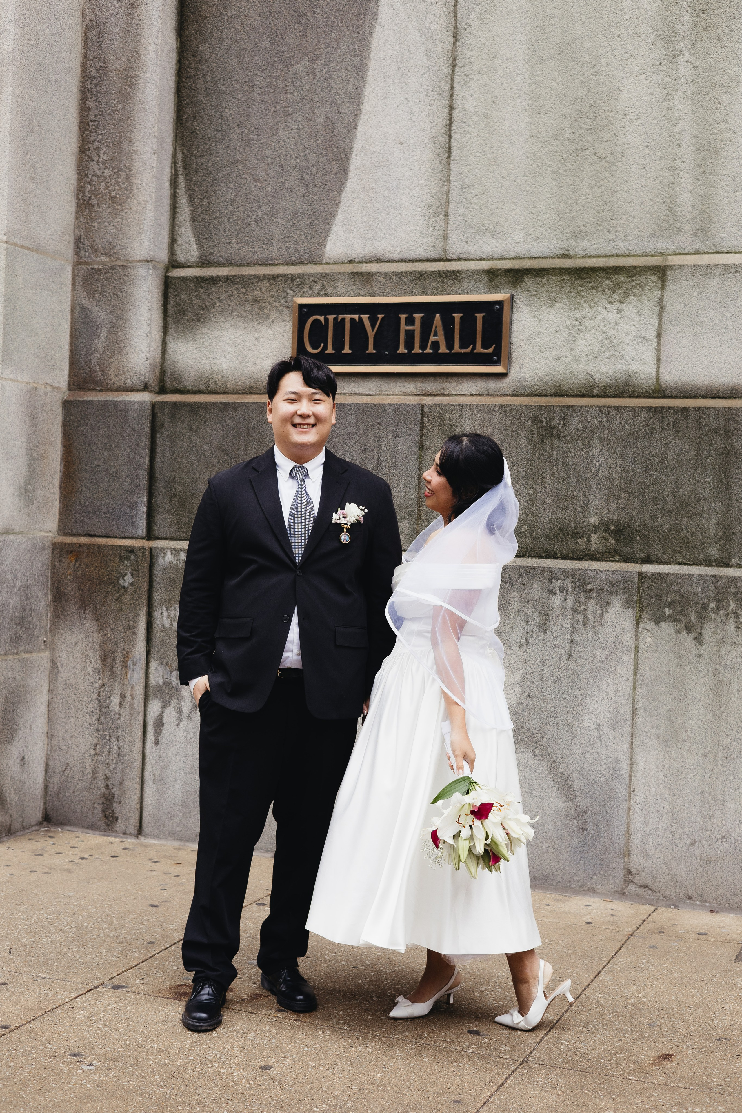 Bride looking at groom while standing in front of the City Hall sign