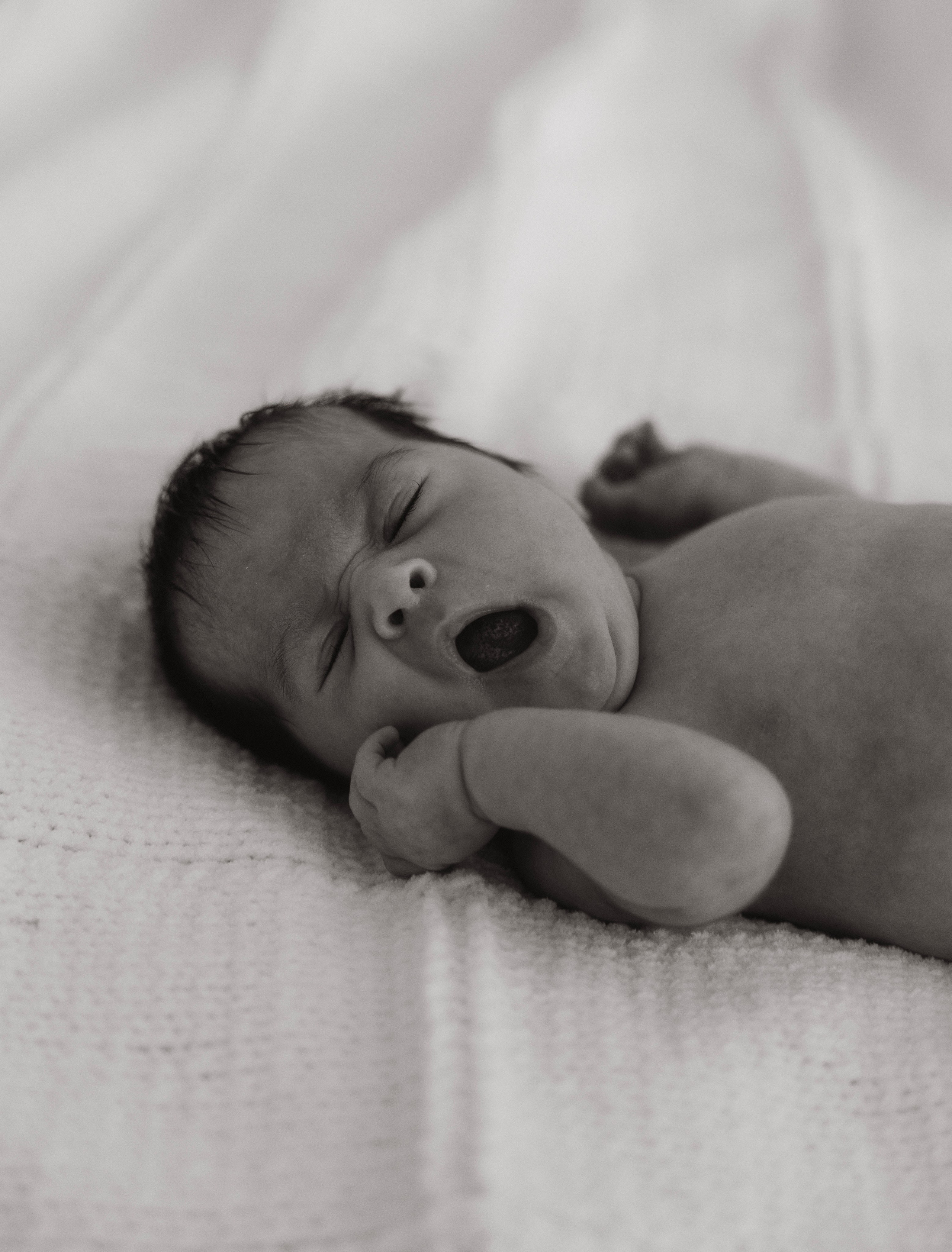 Newborn baby yawning softly in natural light, peaceful and candid moment