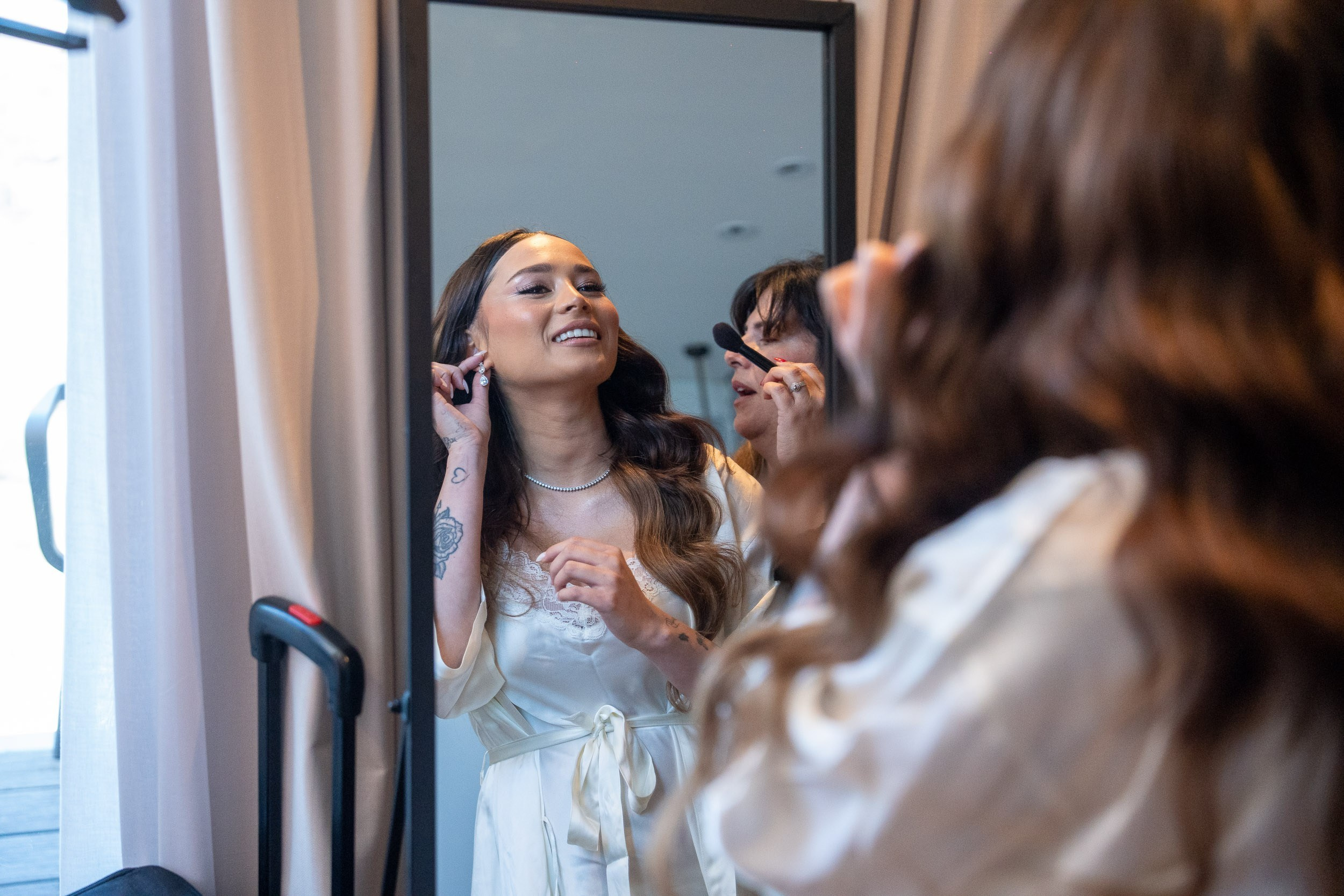 A bride smiles at her reflection while getting ready on the wedding morning