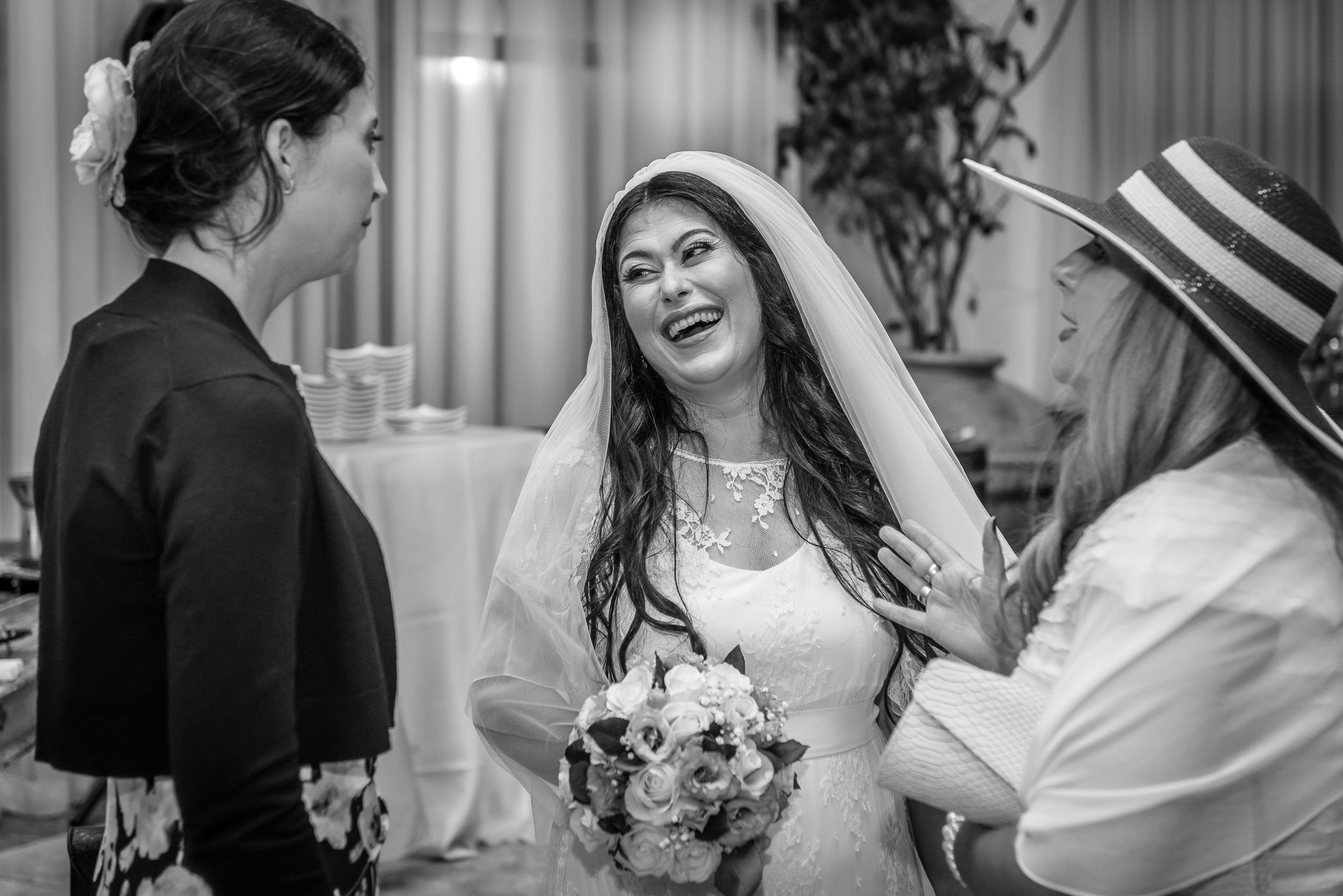 A bride holding her bouquet laughs with guests during the reception