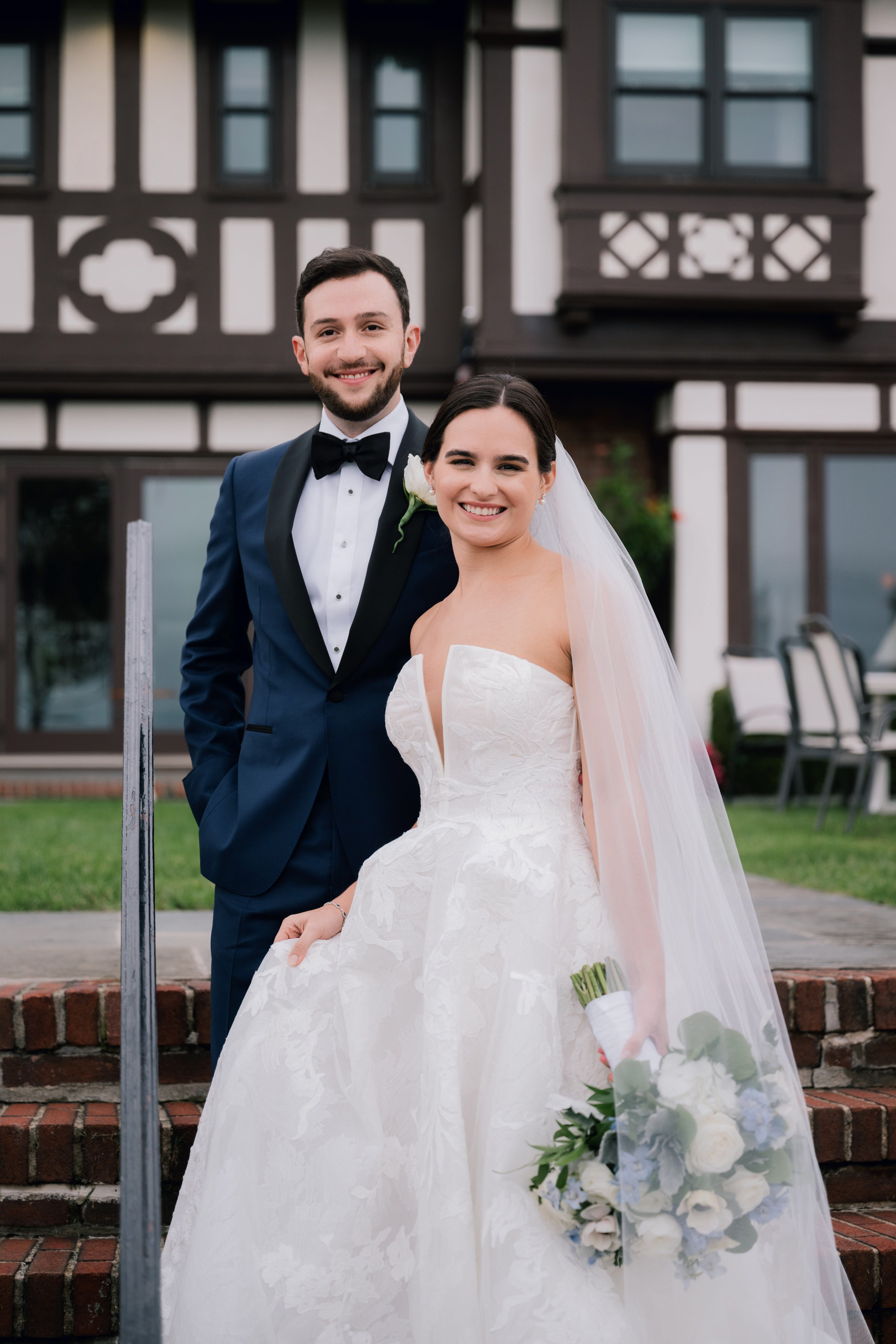 a bride and groom pose for a photo in front of a house