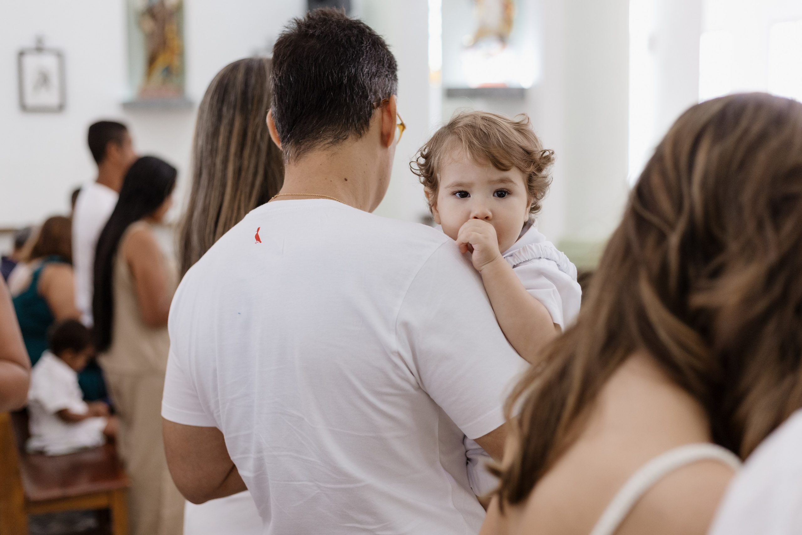 Bebê olhando por cima do ombro do pai durante celebração do batismo