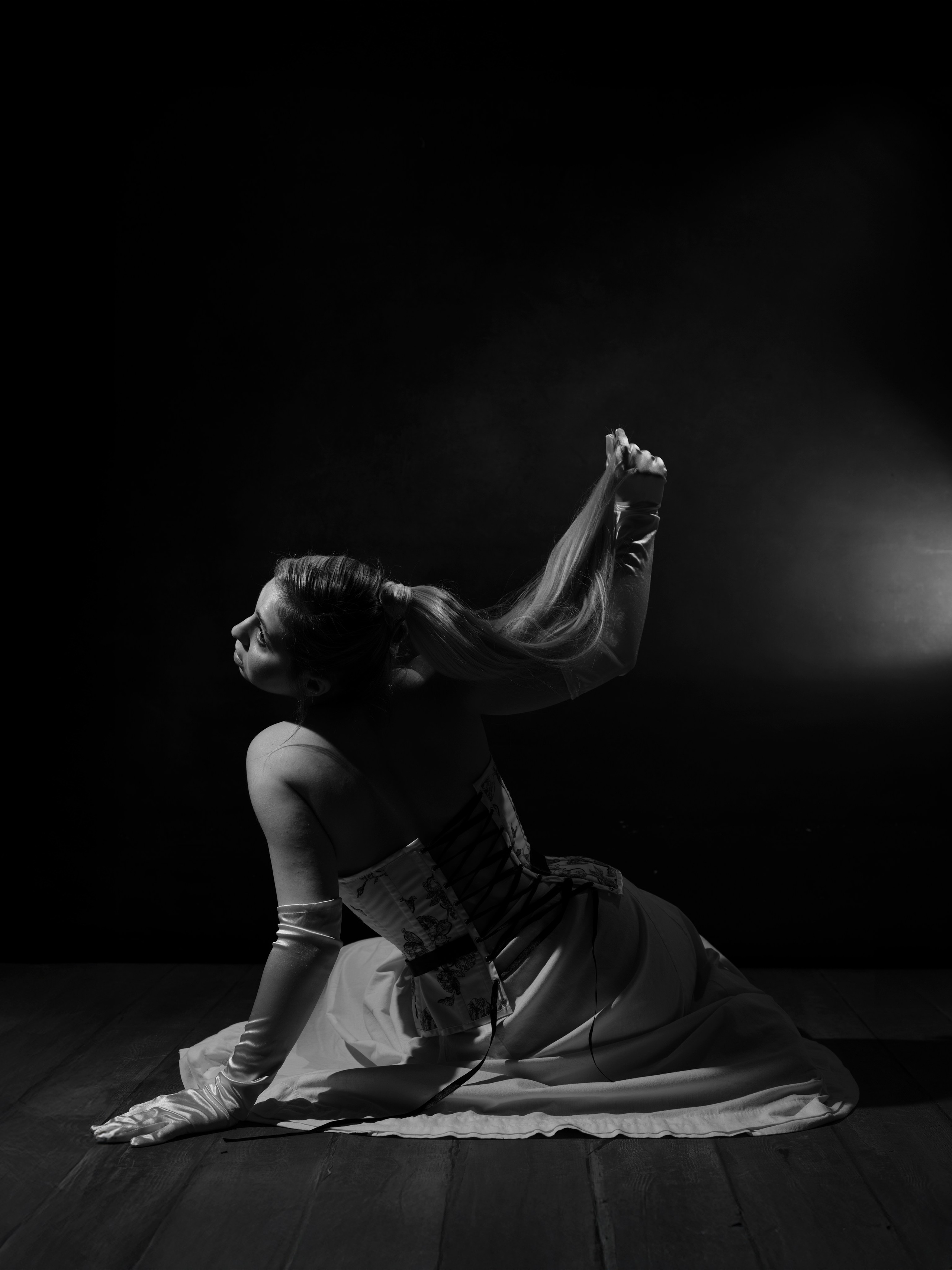A woman sits on a wooden floor and holds a lock of hair in her hand.