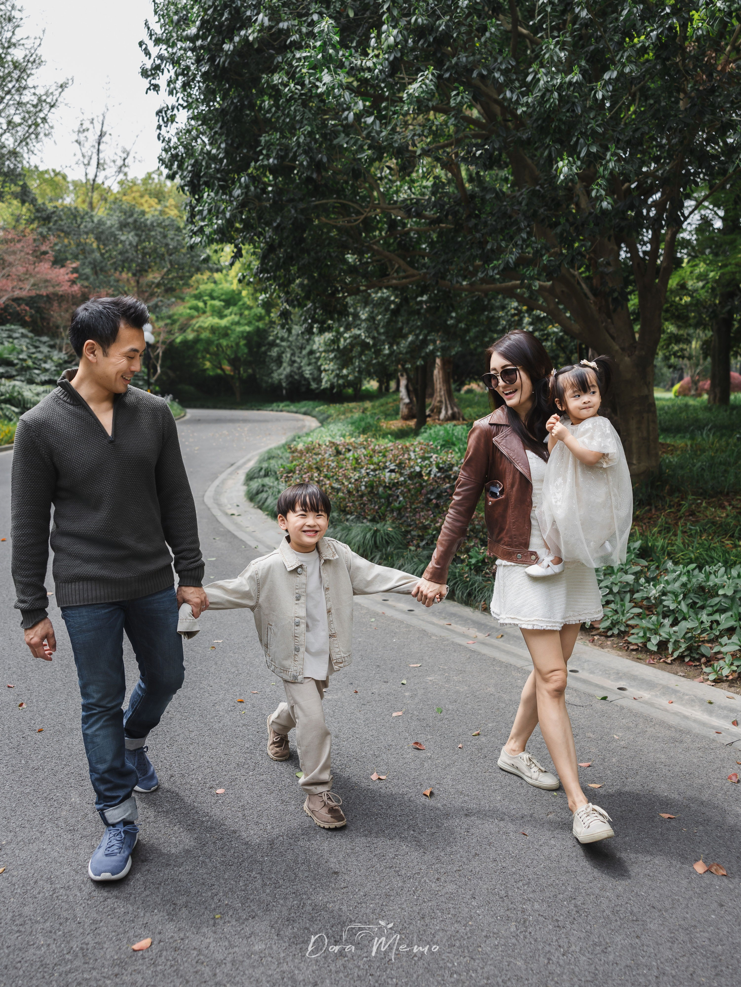 A family of four walking hand in hand along a tree-lined path in Shanghai