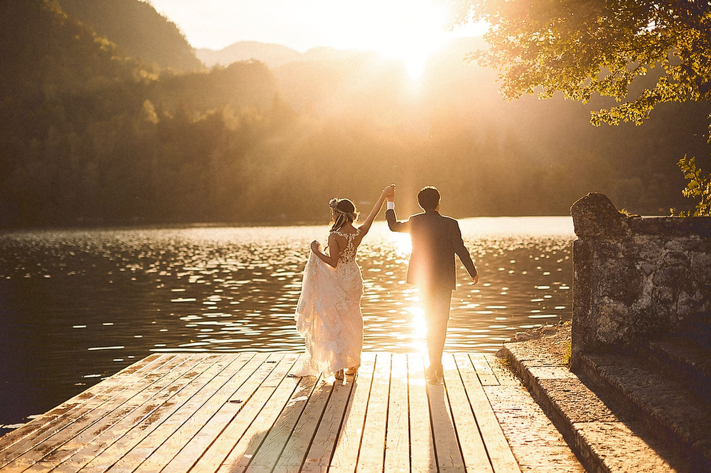 Newlyweds holding their arms up celebrate their union at Bled Island as the late afternoon sun illuminates them.