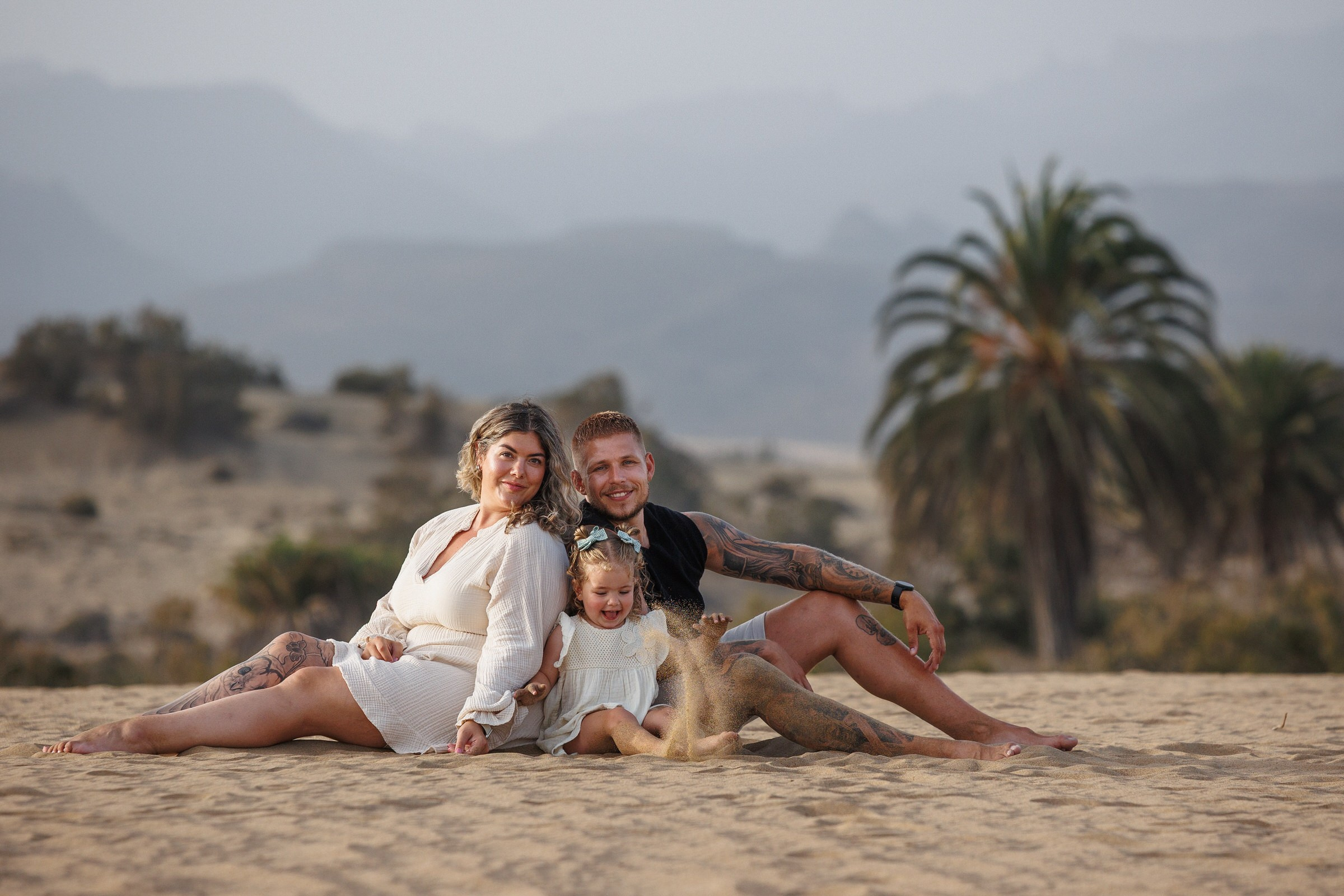 Parents and their toddler sitting together on the sand during a family photoshoot in Maspalomas, Gran Canaria