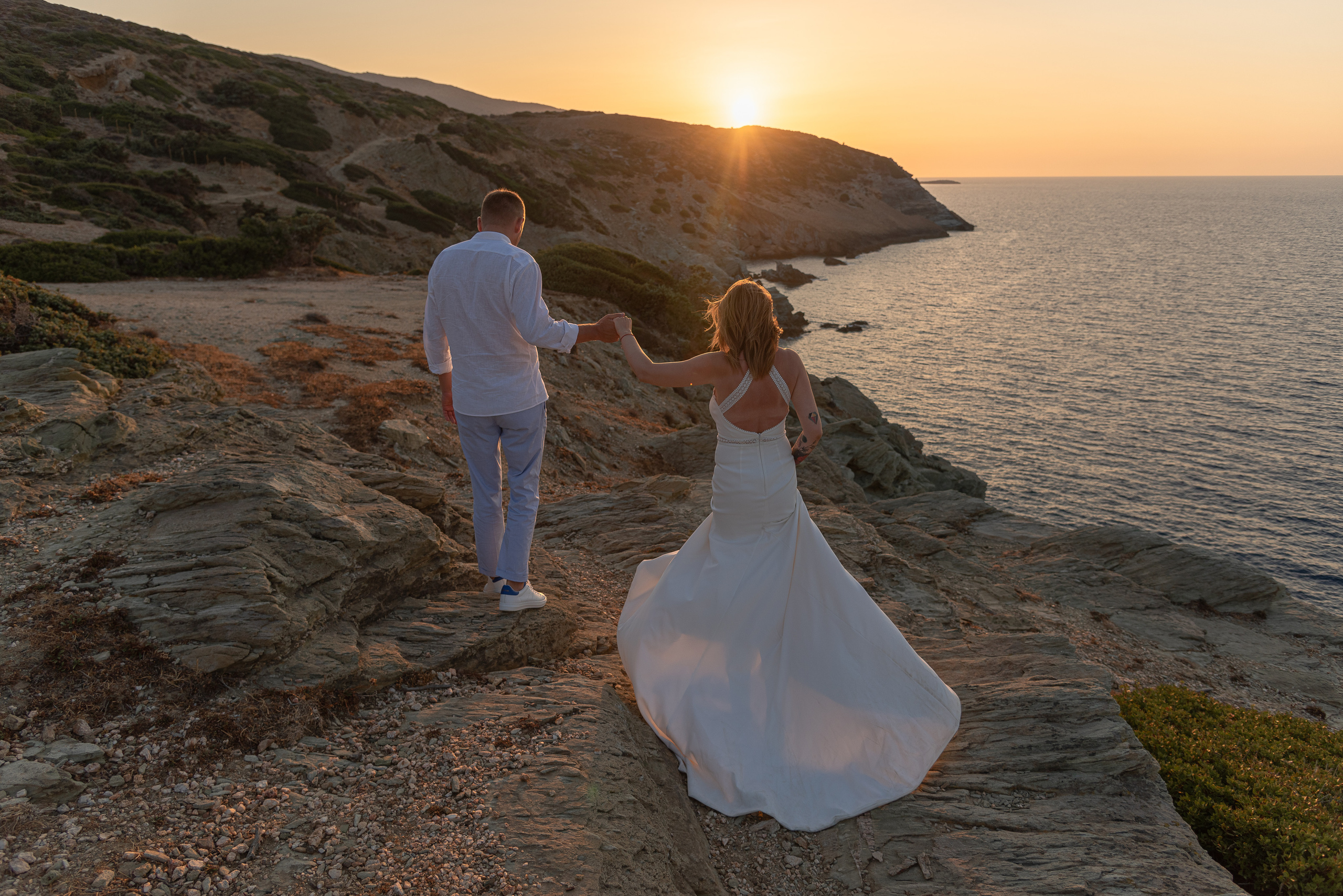 The bride and groom walk along the edge of the abyss at sunset with a view of the sea